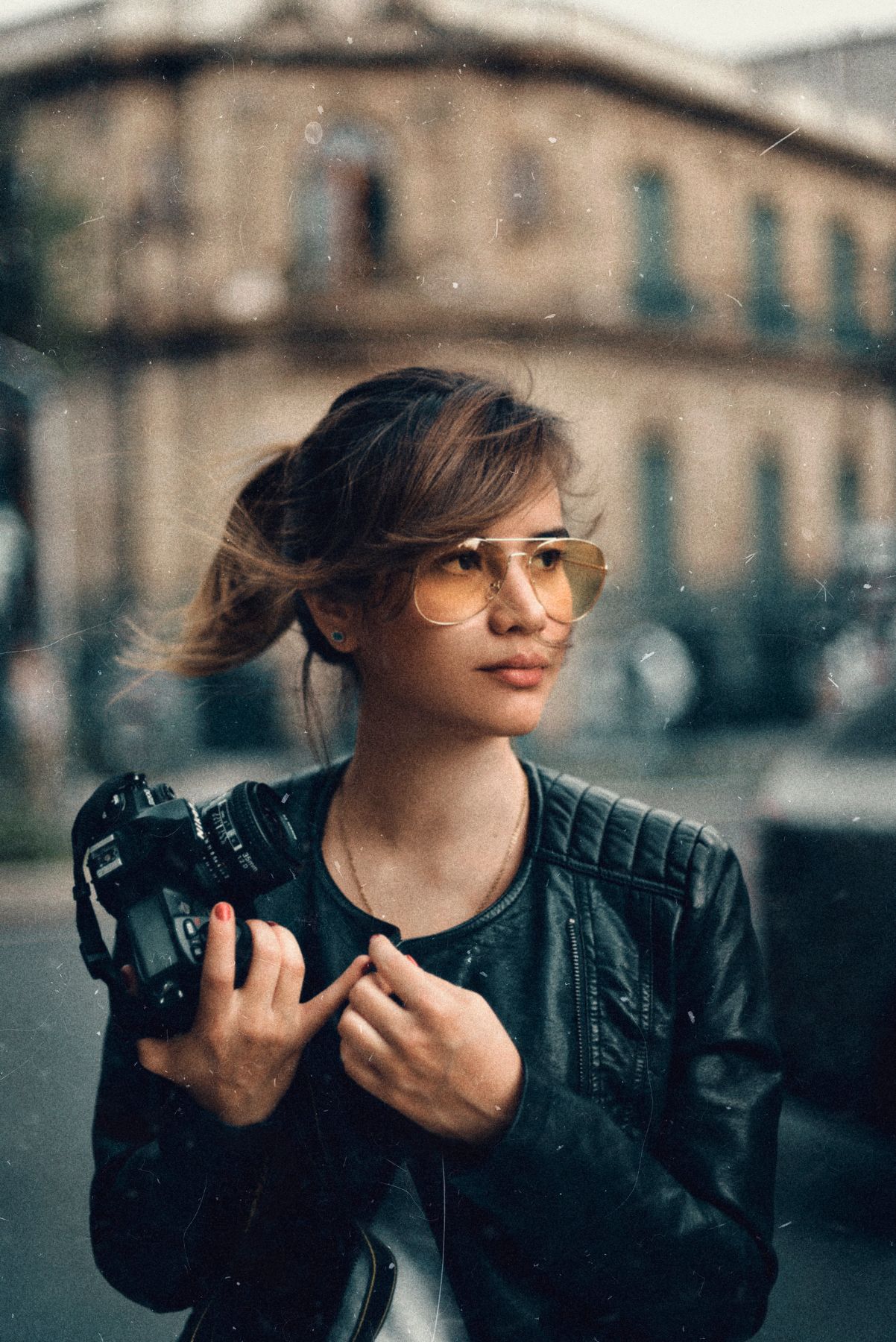 Photographer with aviator sunglasses holding camera in urban setting.