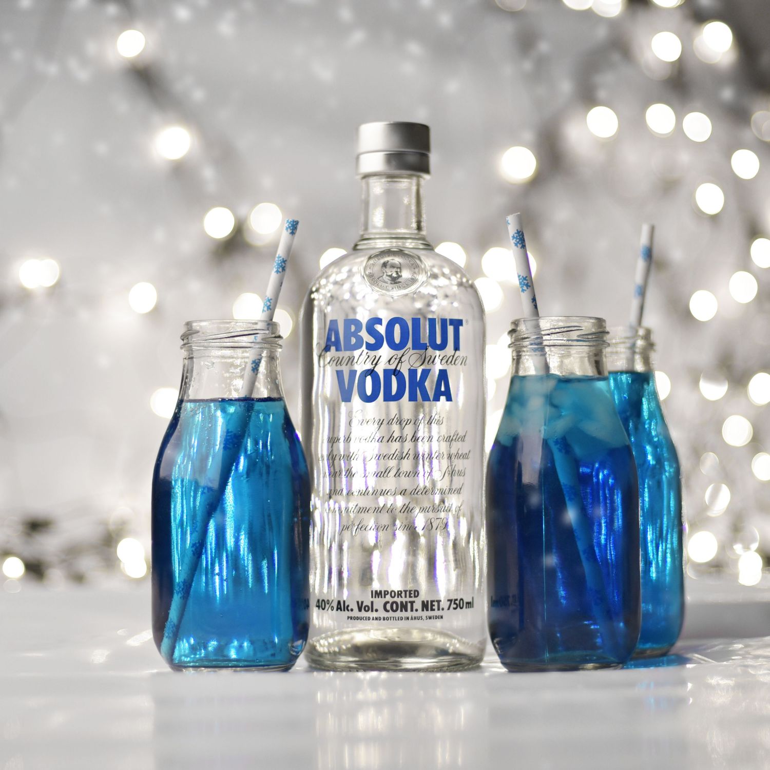 Absolut vodka bottle with blue cocktails in mason jars against sparkly background.