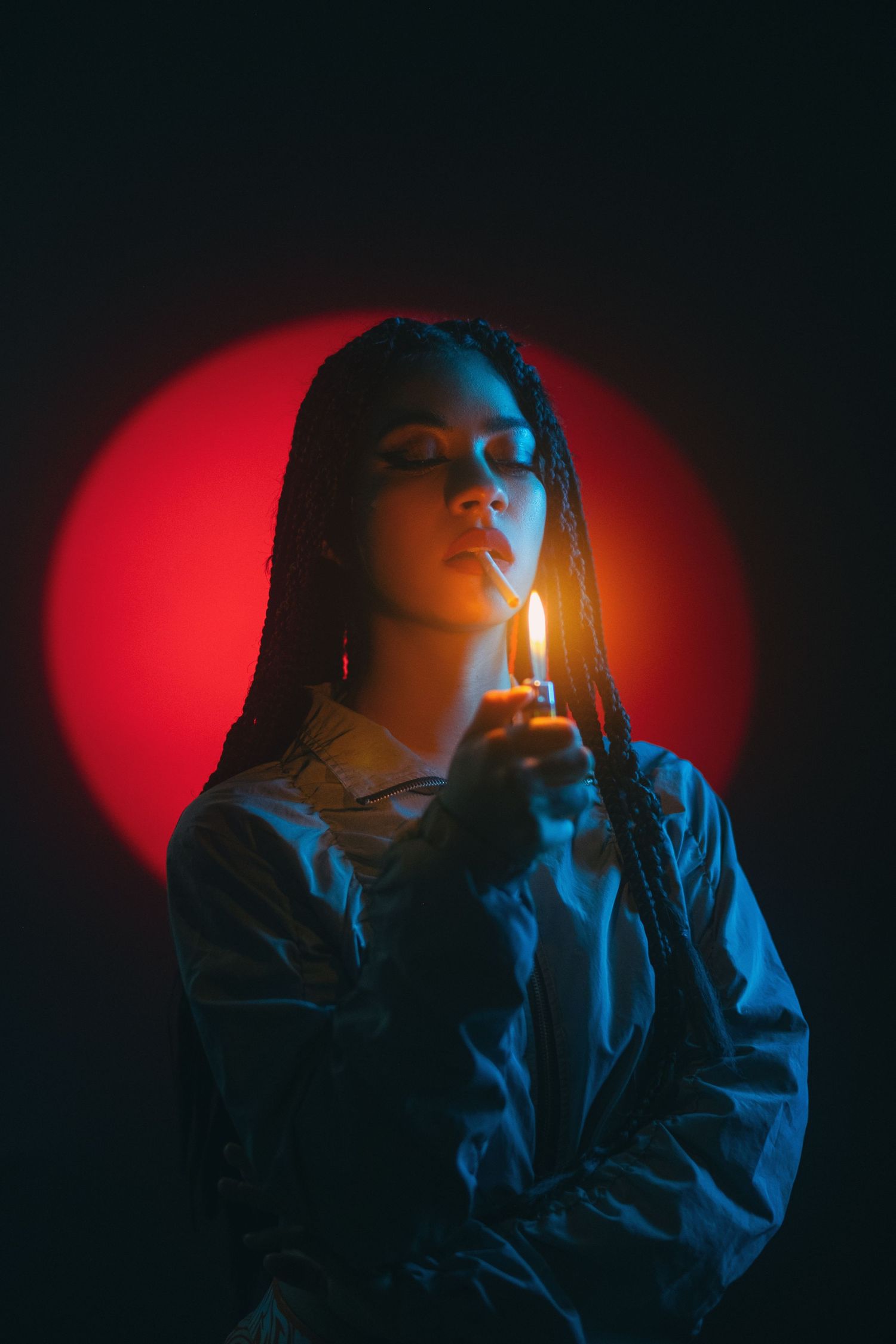 Dramatic portrait with woman lighting match against red circular backdrop.