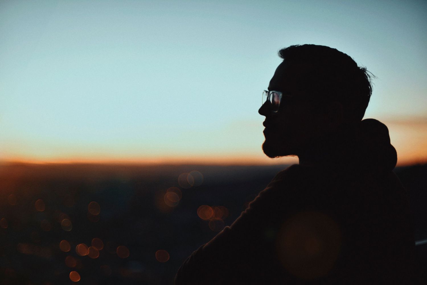 Silhouette of person in sunglasses against sunset sky.