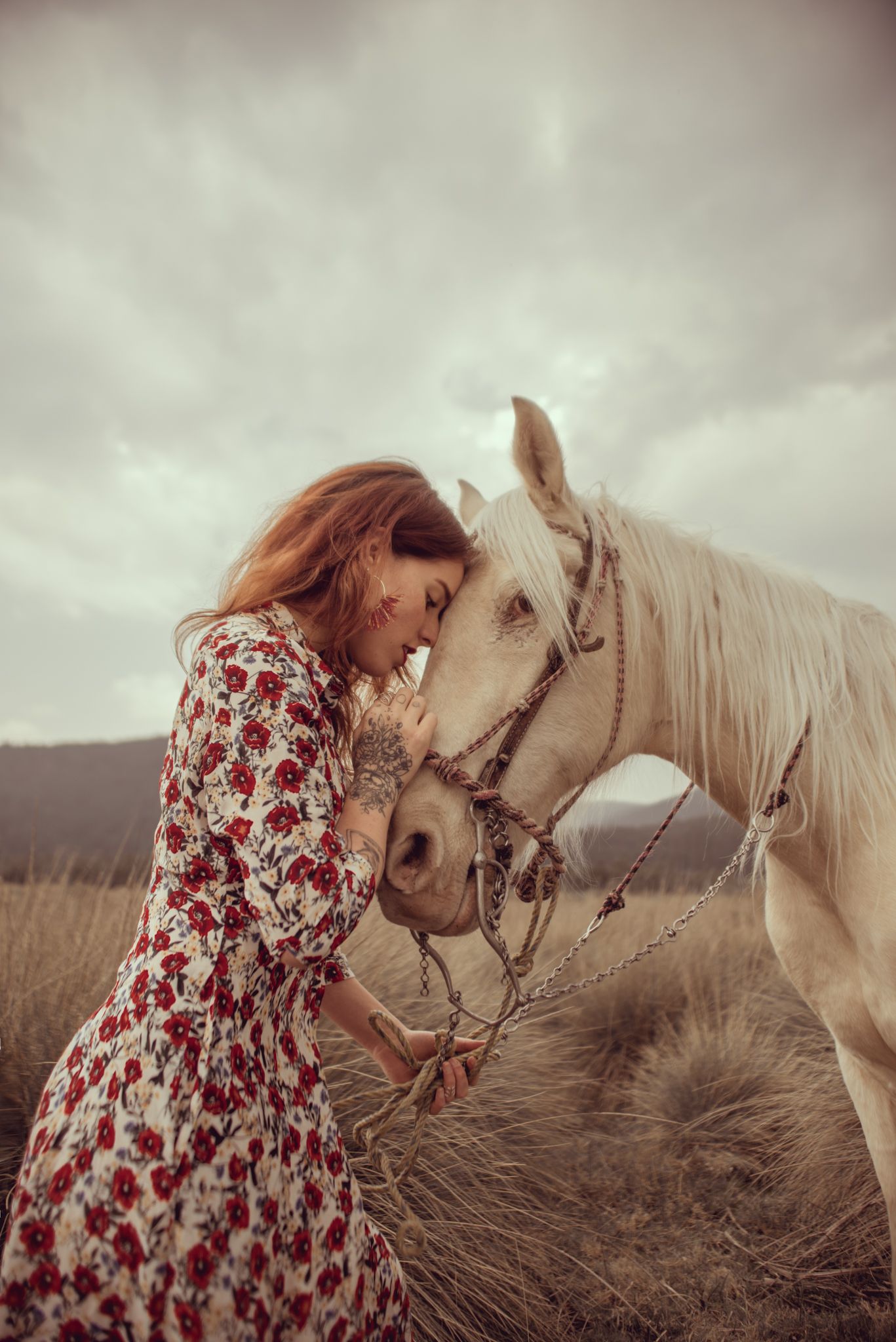 Romantic scene of a woman in floral dress sharing an intimate moment with a white horse in a misty field.