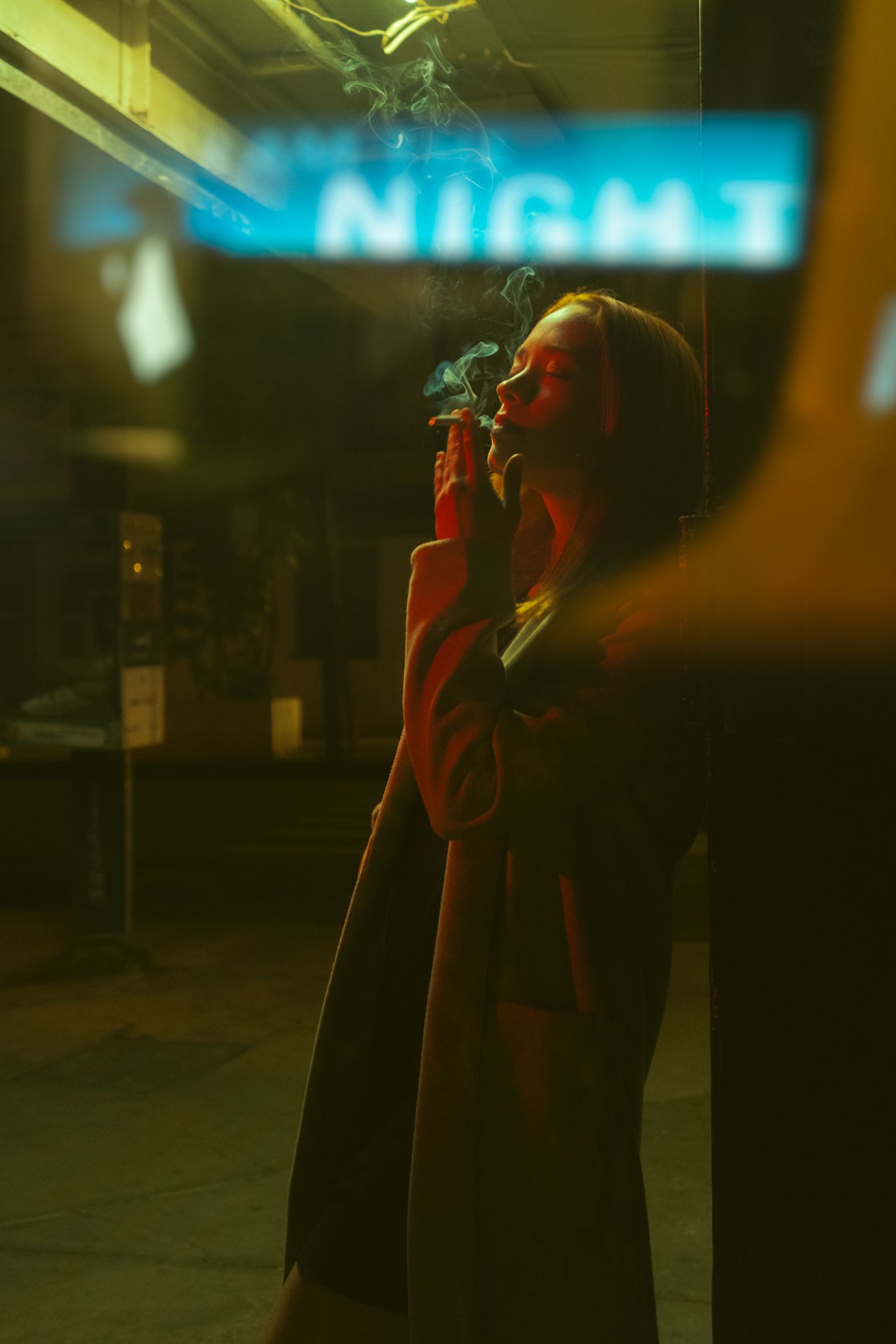 Silhouette standing beneath neon blue 'NIGHT' sign in moody urban setting with red lighting.