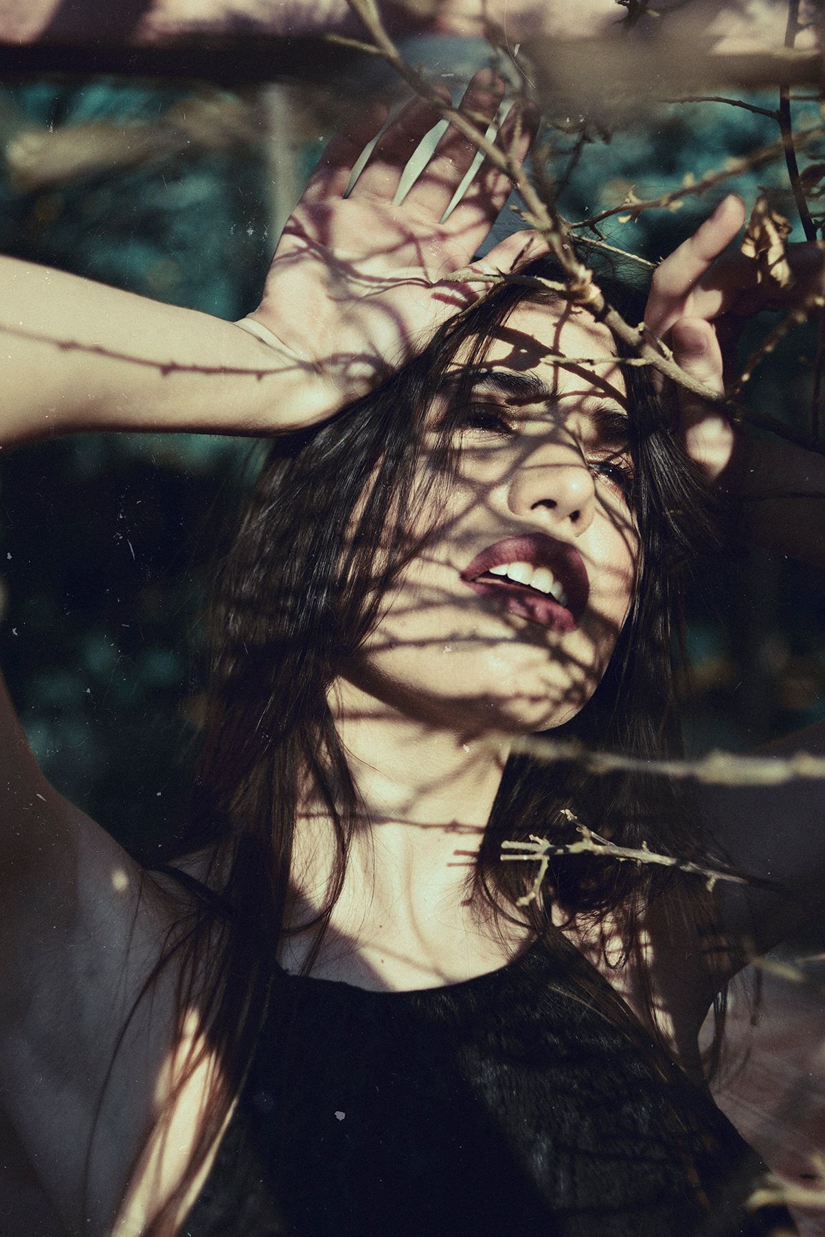 Dramatic portrait with shadows from branches creating patterns across face.