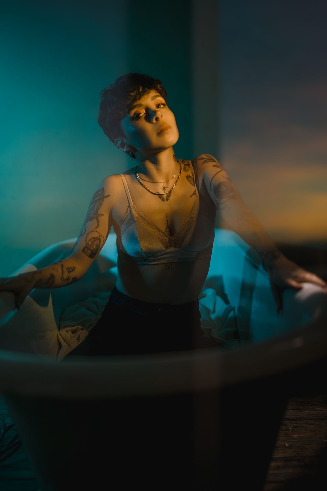 Artistic portrait in tank top with teal and amber lighting creating moody atmosphere.