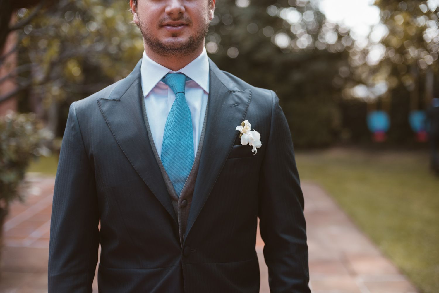 A formal wedding portrait showing a navy suit with light blue tie and white boutonniere detail.