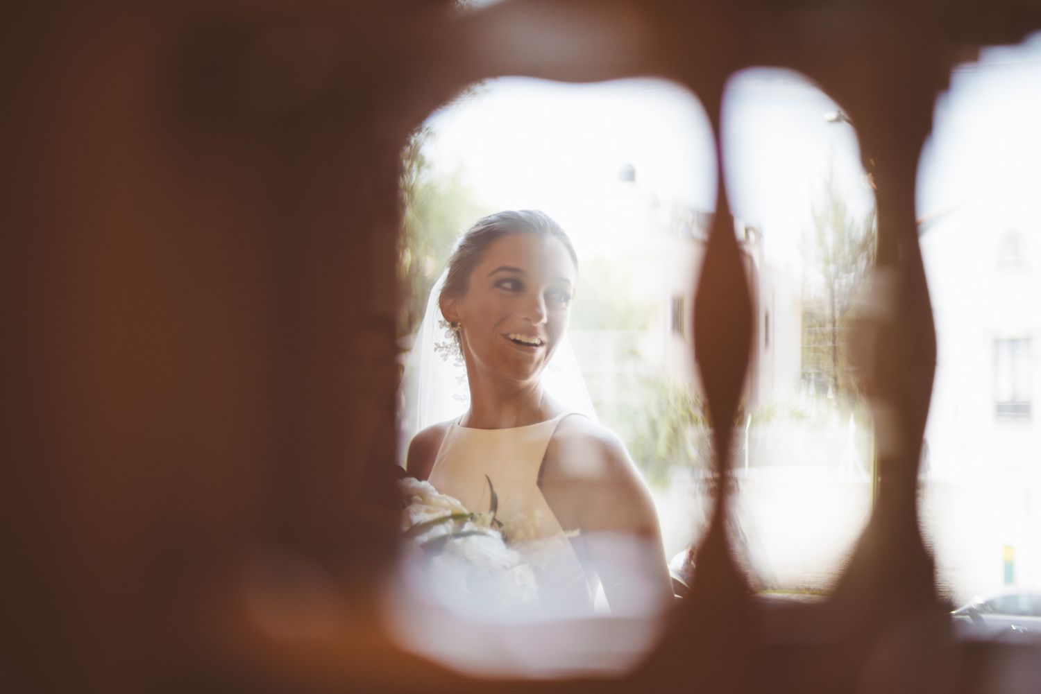 An artistic shot through an architectural detail shows a person in white wedding attire.