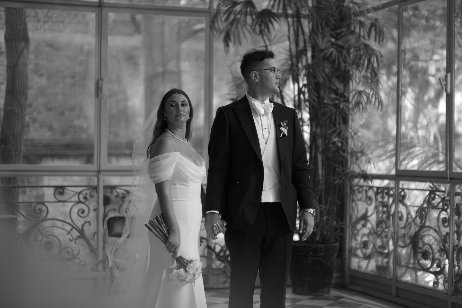 Elegant bride and groom standing together in a sunlit conservatory space.