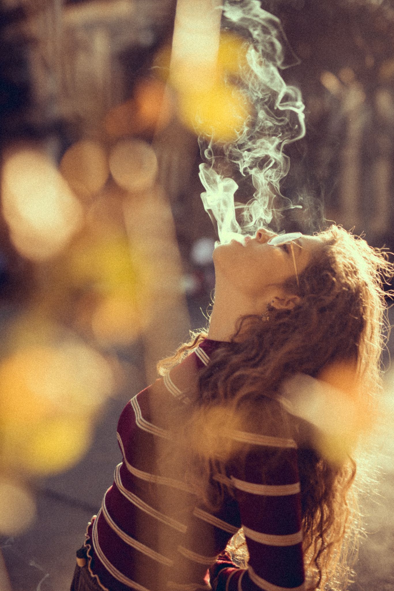 Artistic smoke photography with model in striped clothing against blurred golden background.