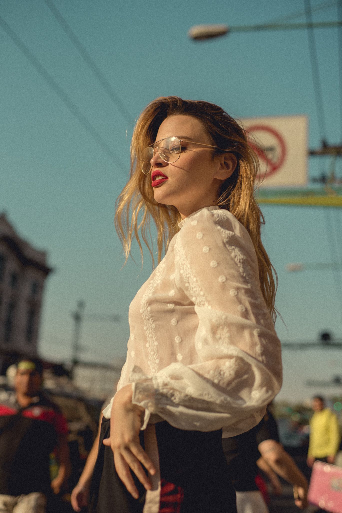 Fashion portrait with vintage white blouse and glasses against urban skyline and street signs.