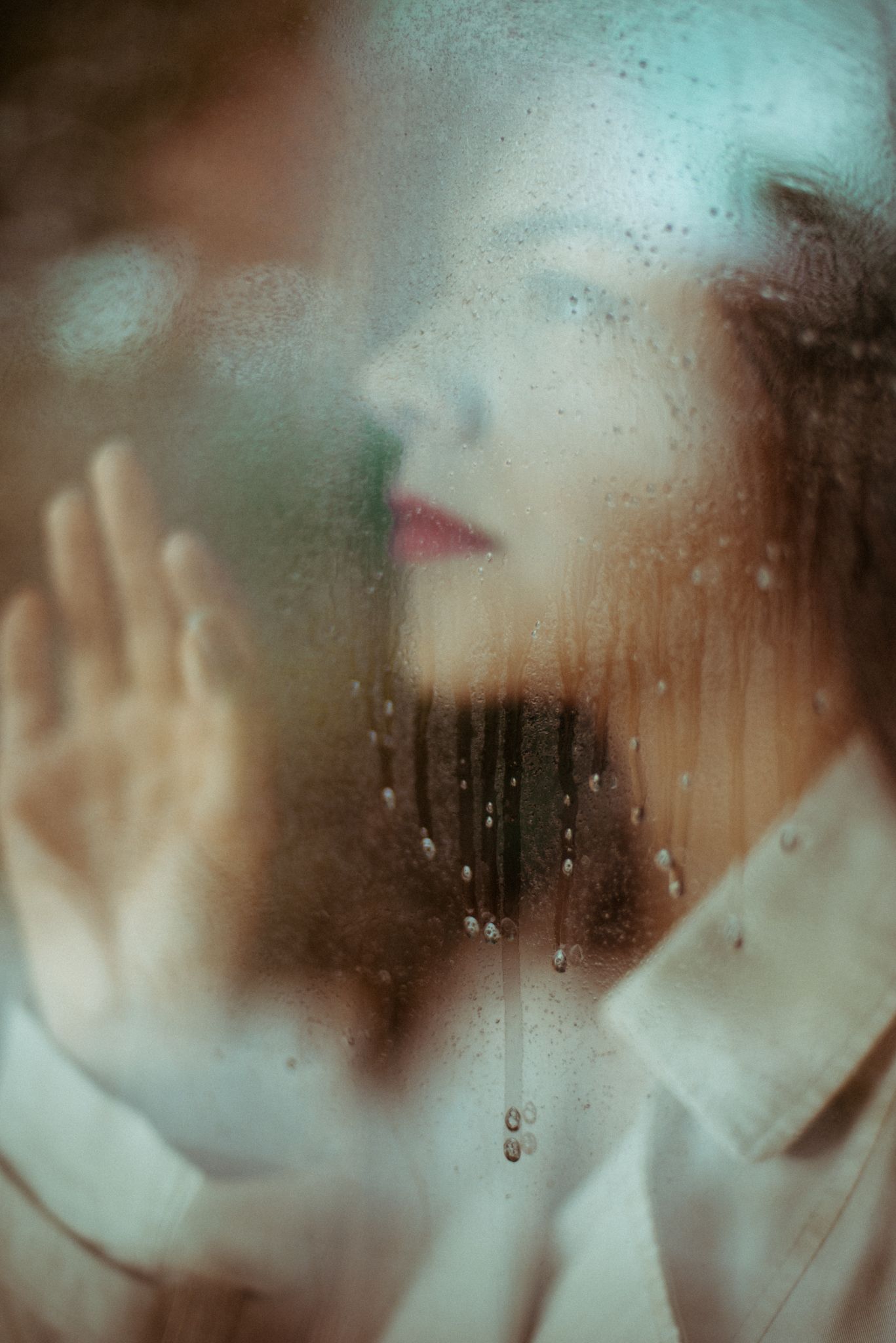 Dreamy portrait through foggy glass with water droplets and soft focus.
