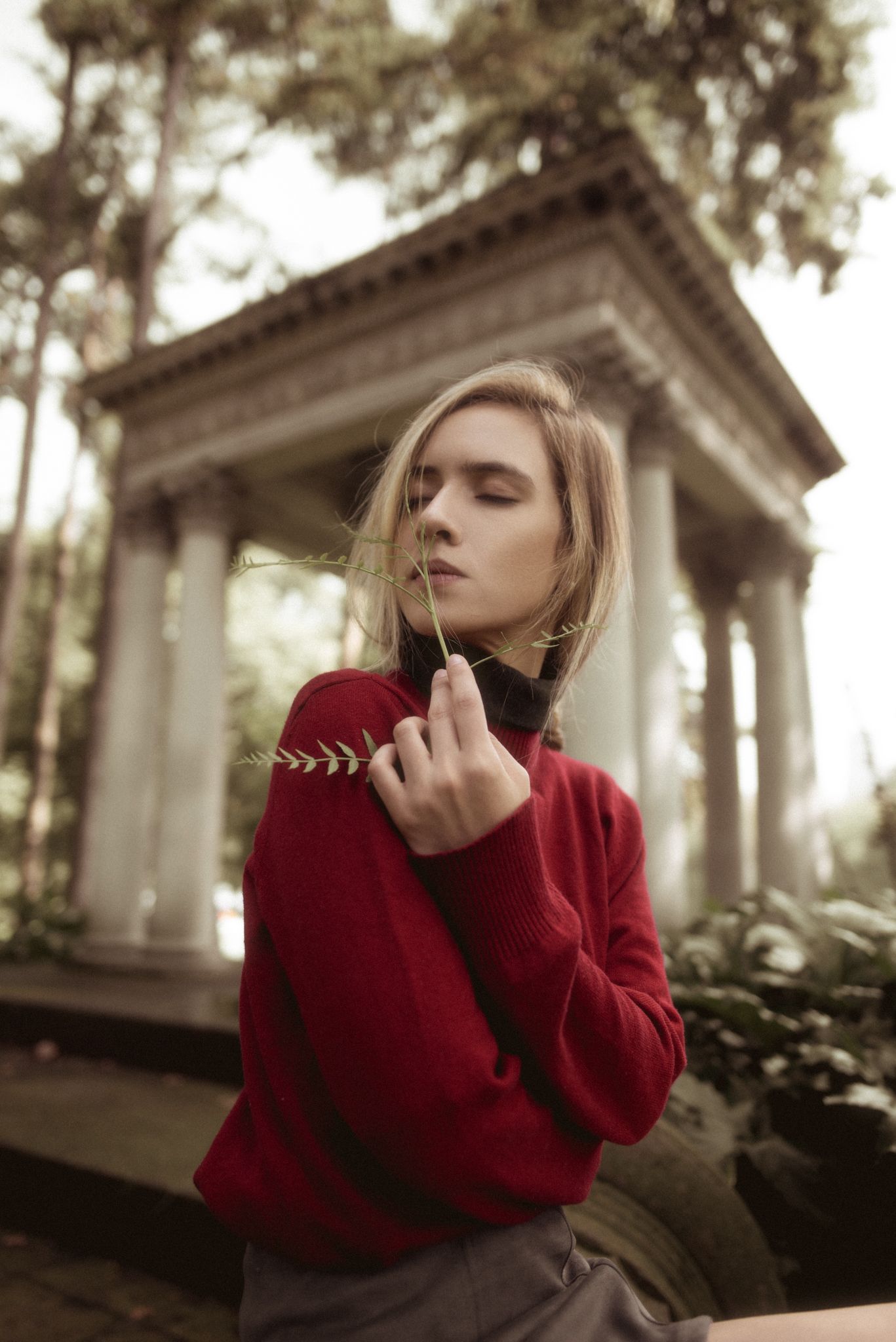 Fashion portrait of model in red sweater posing near classical architecture in autumn setting.