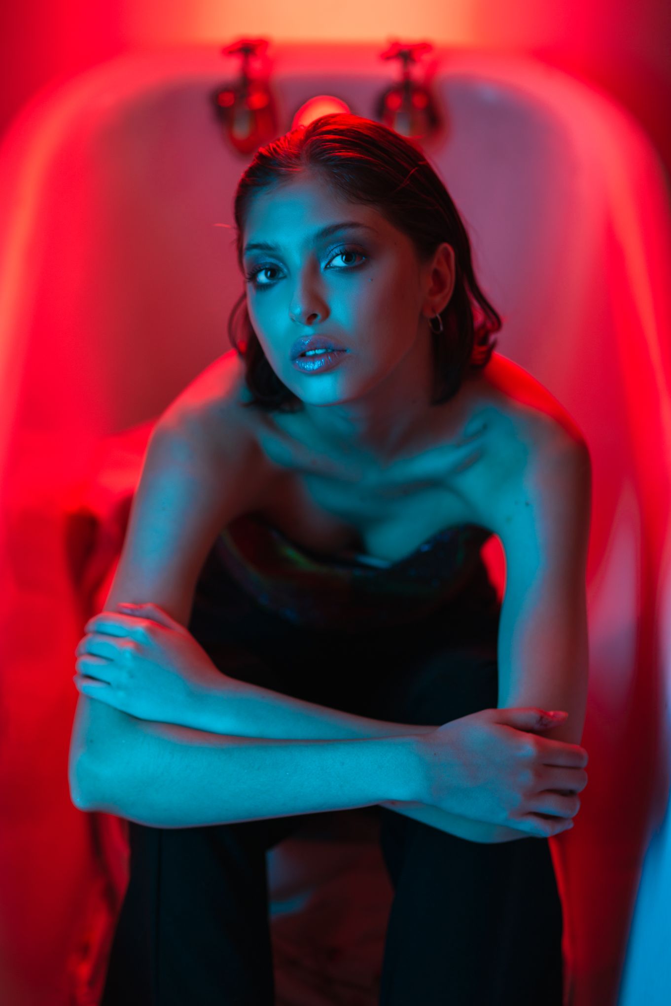 Dramatic portrait in bathtub with red and blue neon lighting.