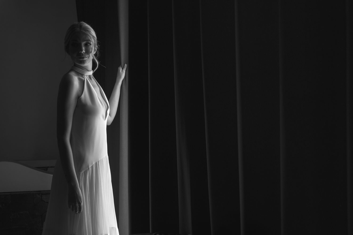 A dramatic black and white portrait shows a figure in an elegant white gown standing by flowing curtains.