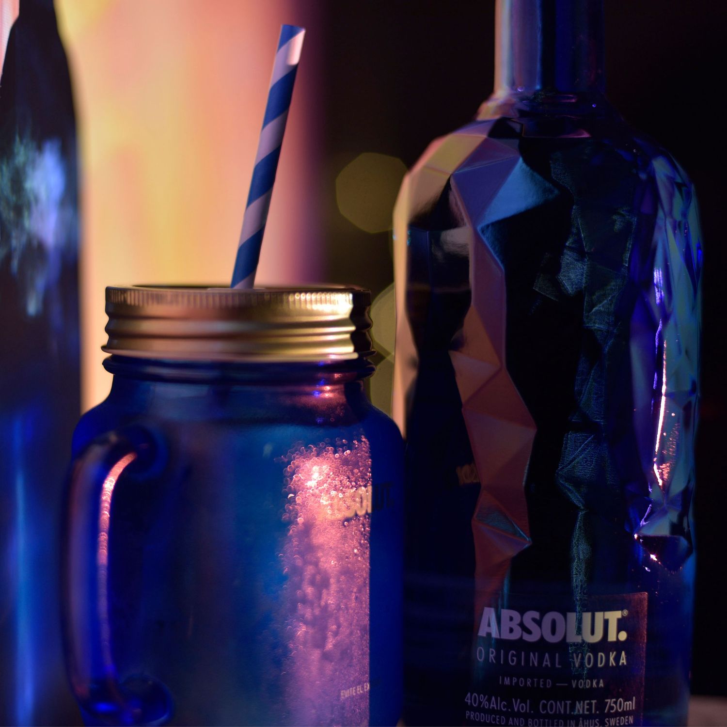Blue and pink illuminated glass jar with liquid against dark background creates moody nightclub atmosphere.