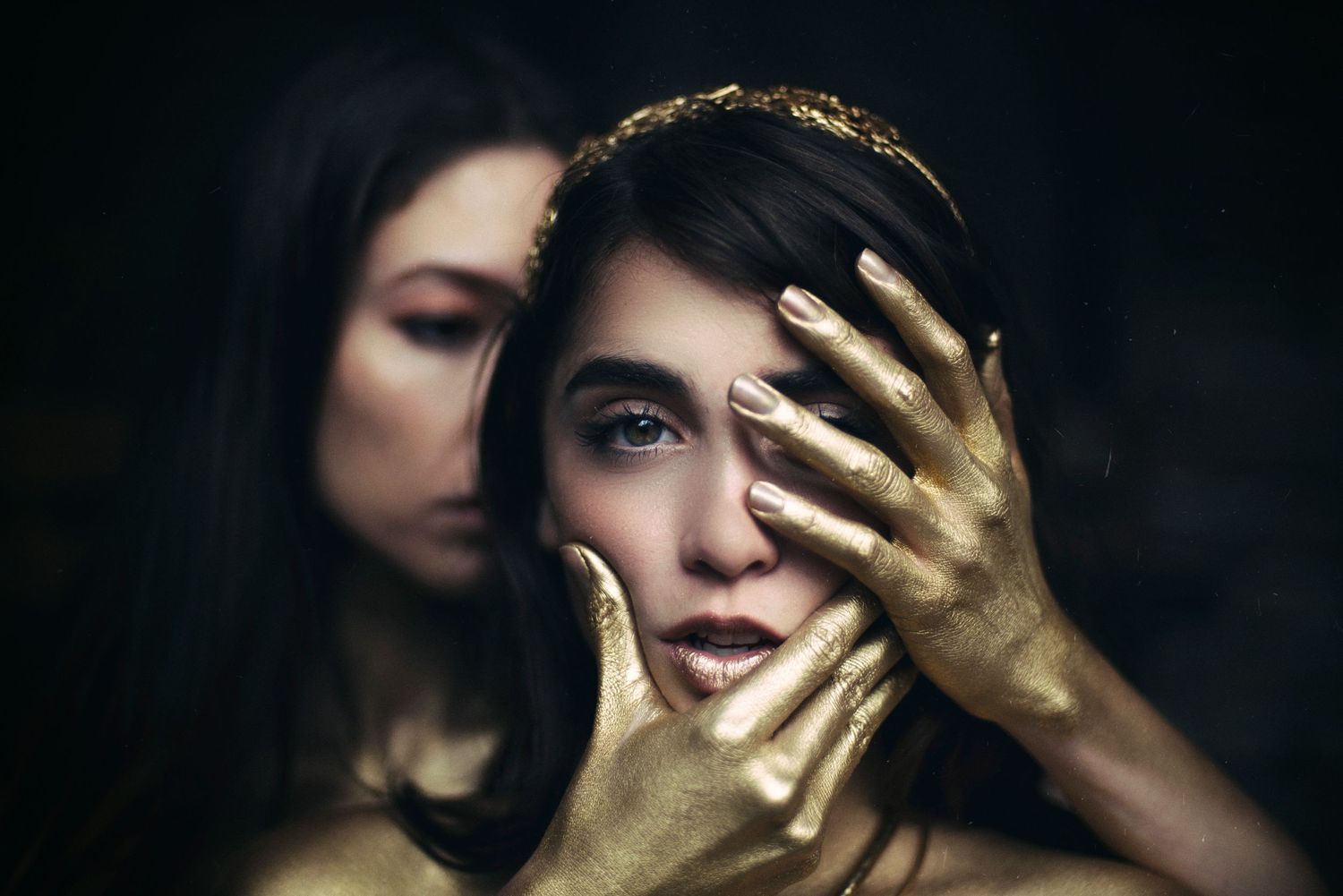 Artistic portrait with golden hands creating shadows and dramatic lighting effects.