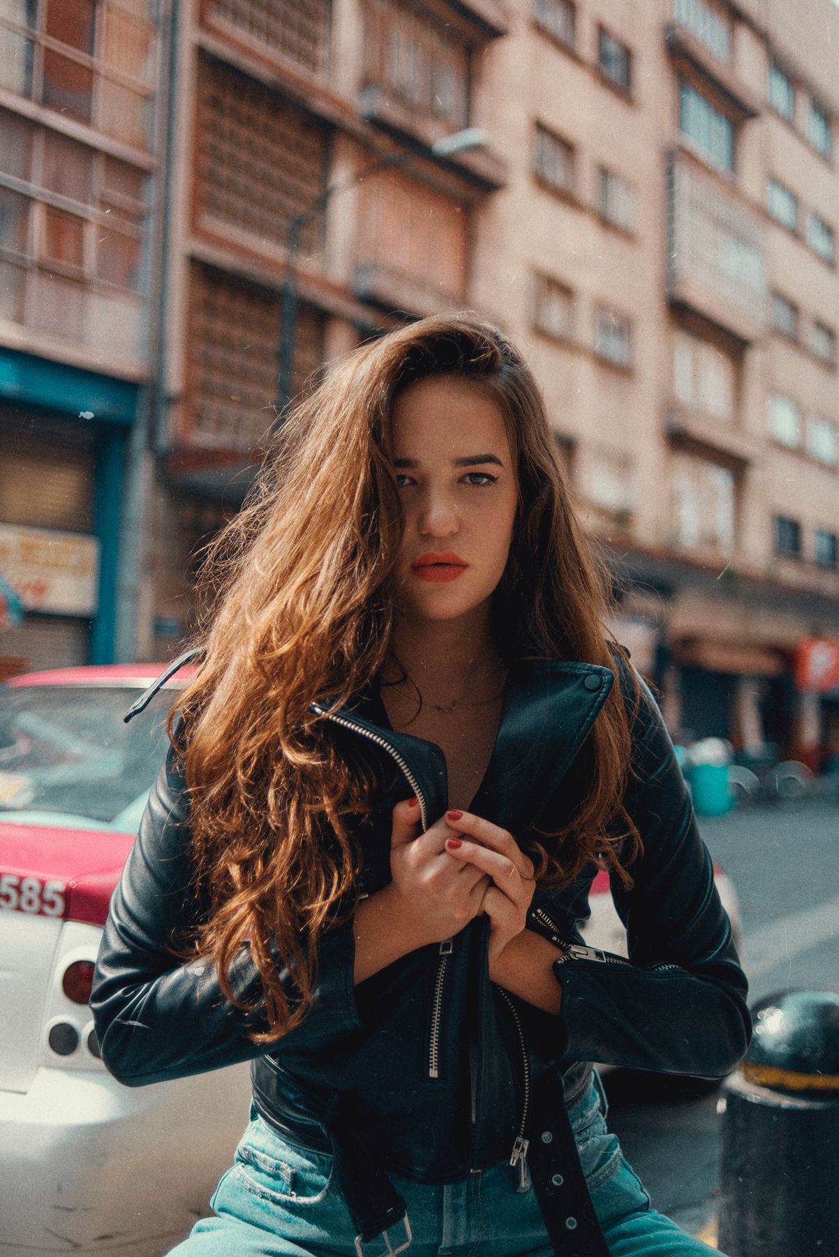Urban fashion portrait with leather jacket against city backdrop with moody lighting.