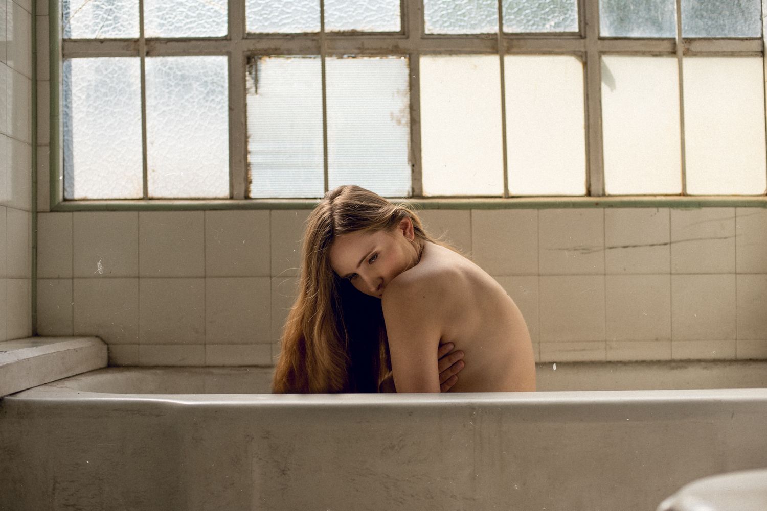 Artistic portrait of a person sitting in a vintage bathtub near a window.