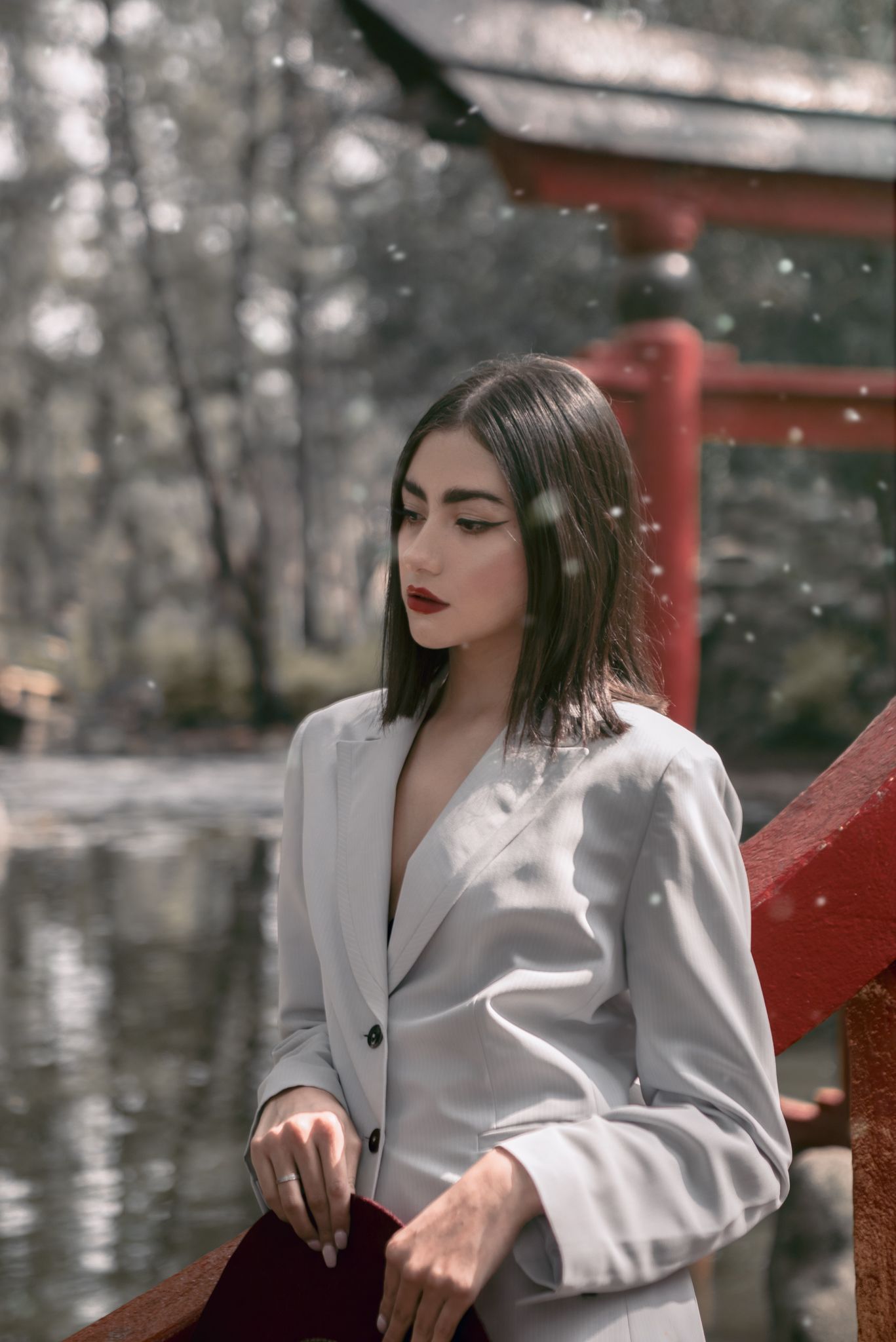 Winter portrait in white blazer near red Japanese torii gate with falling snow.