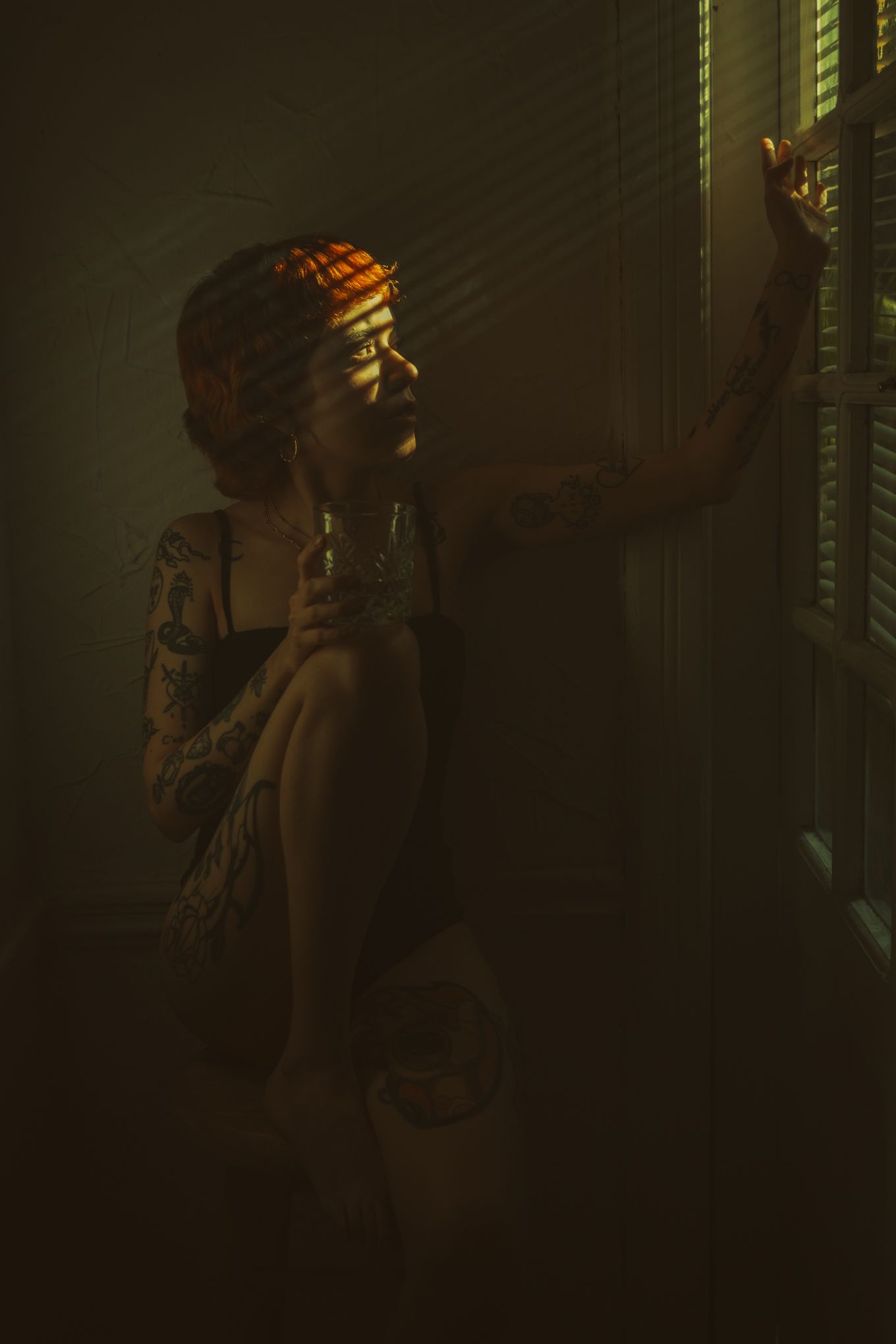 Moody portrait in shadow with light streaming through window blinds.