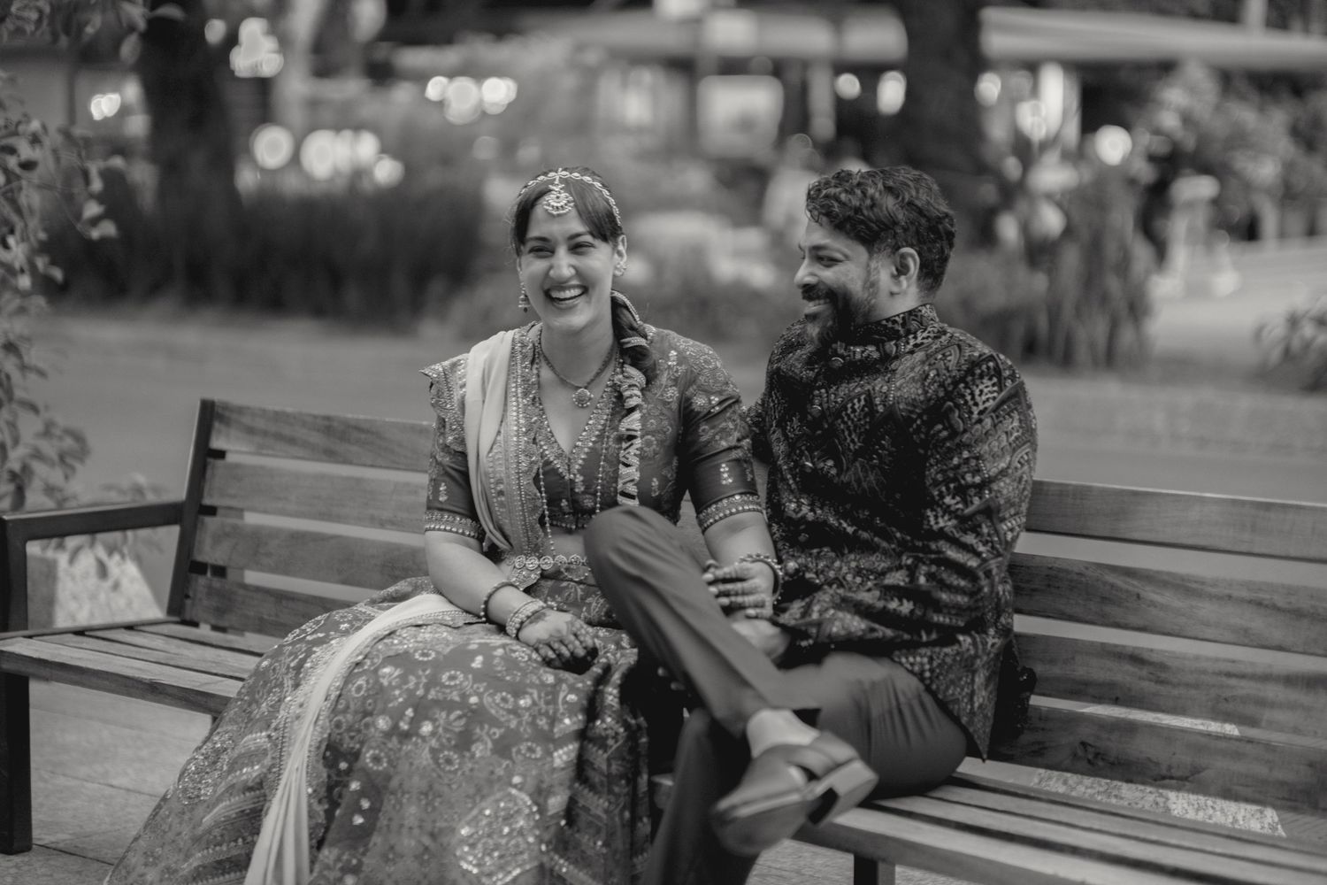 Couple in traditional Indian wedding attire sharing intimate moment on park bench.