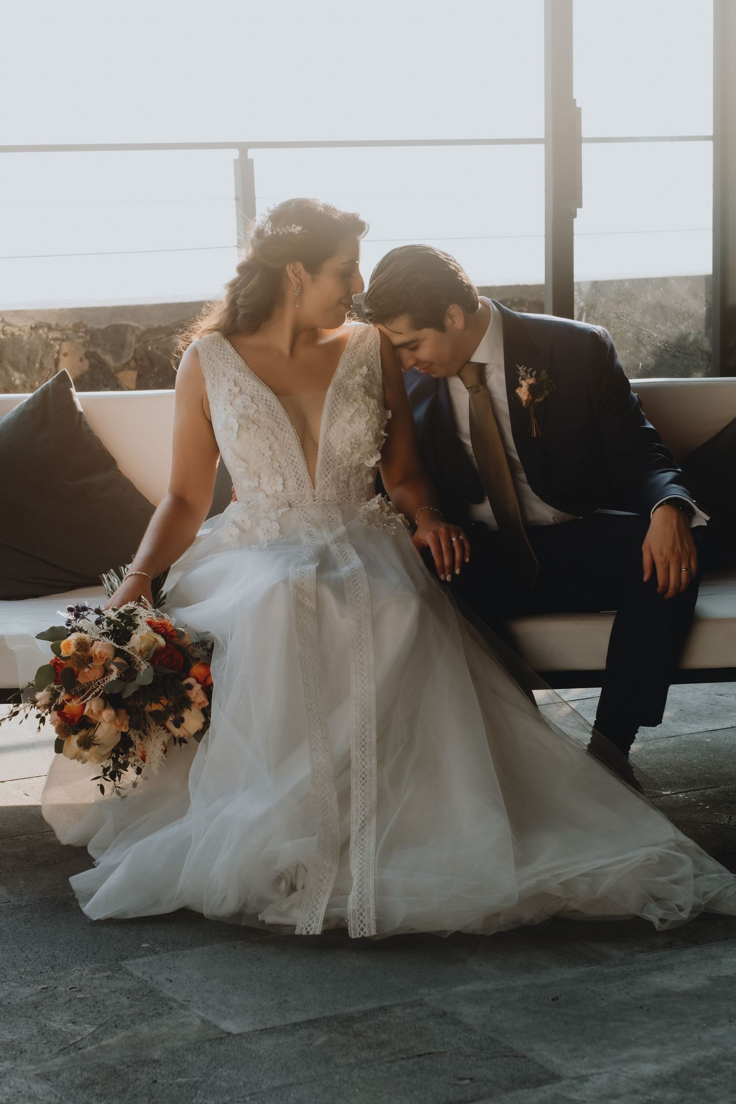 A couple shares an intimate moment on a couch during their wedding day.