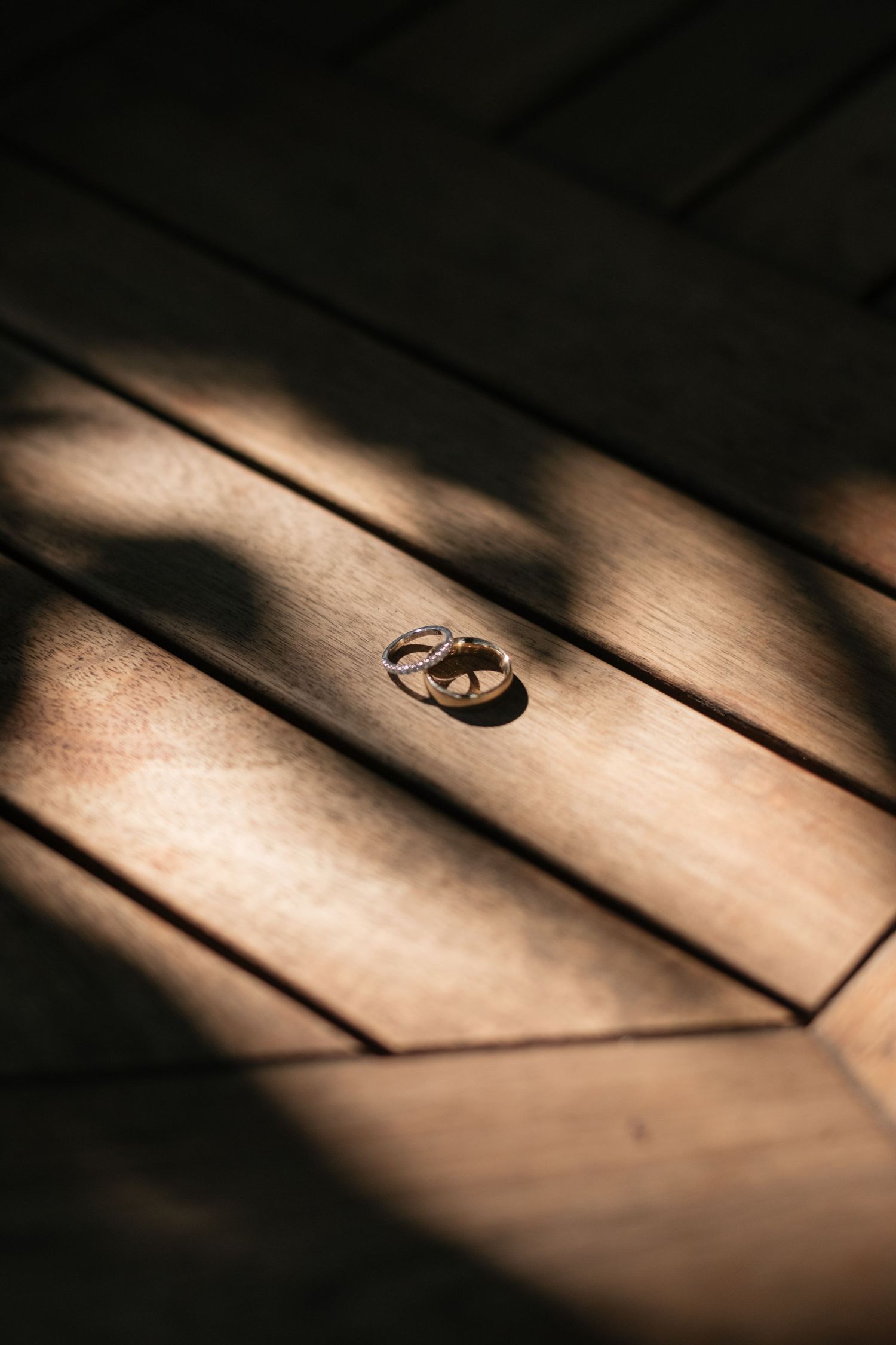 Wedding rings casting dramatic shadows on wooden planks in moody lighting.