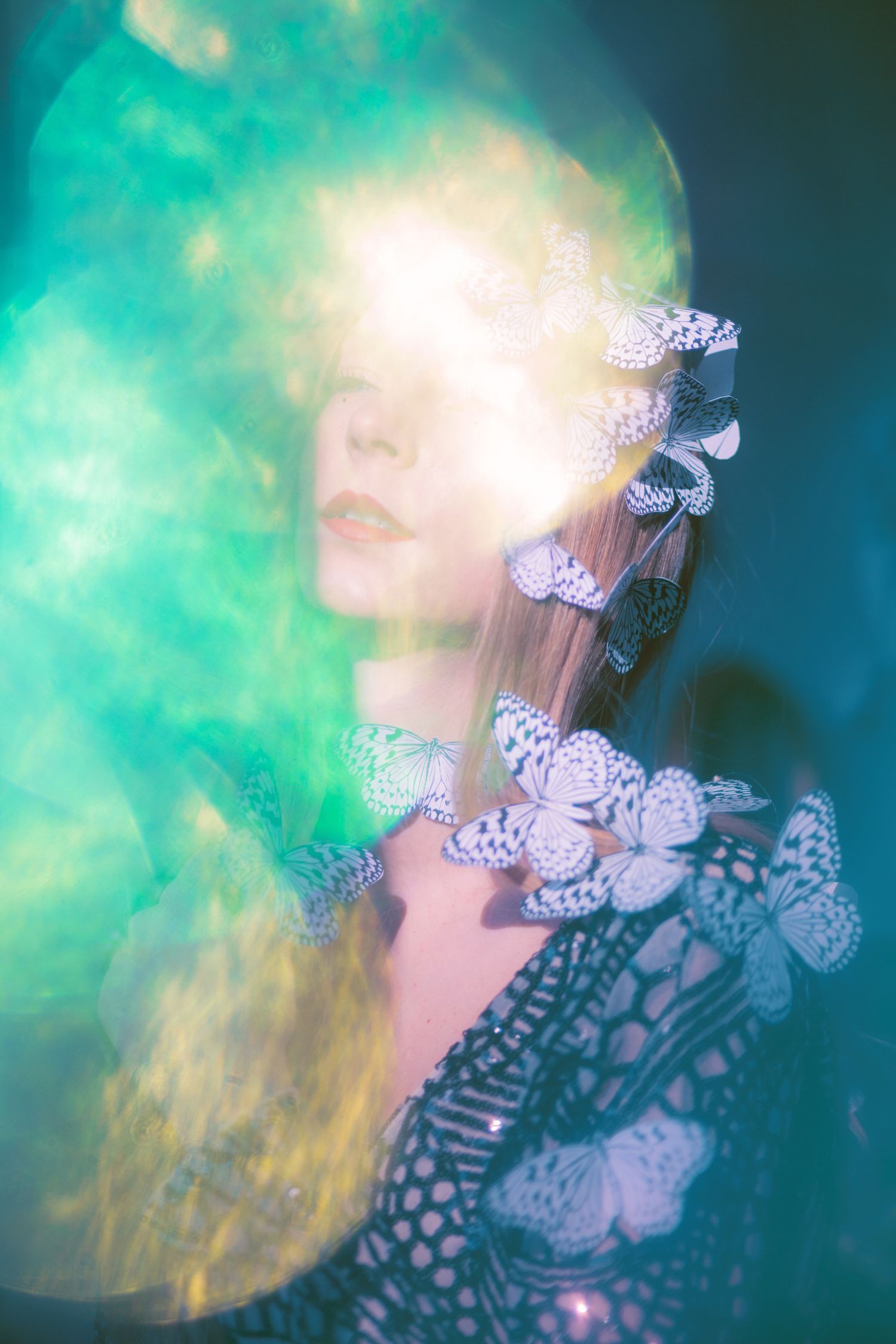 Dreamy portrait with delicate white butterflies against turquoise backdrop and ethereal lighting effects.