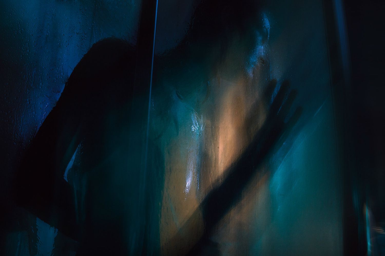 Mysterious silhouette behind glass with blue lighting and hand shadow.