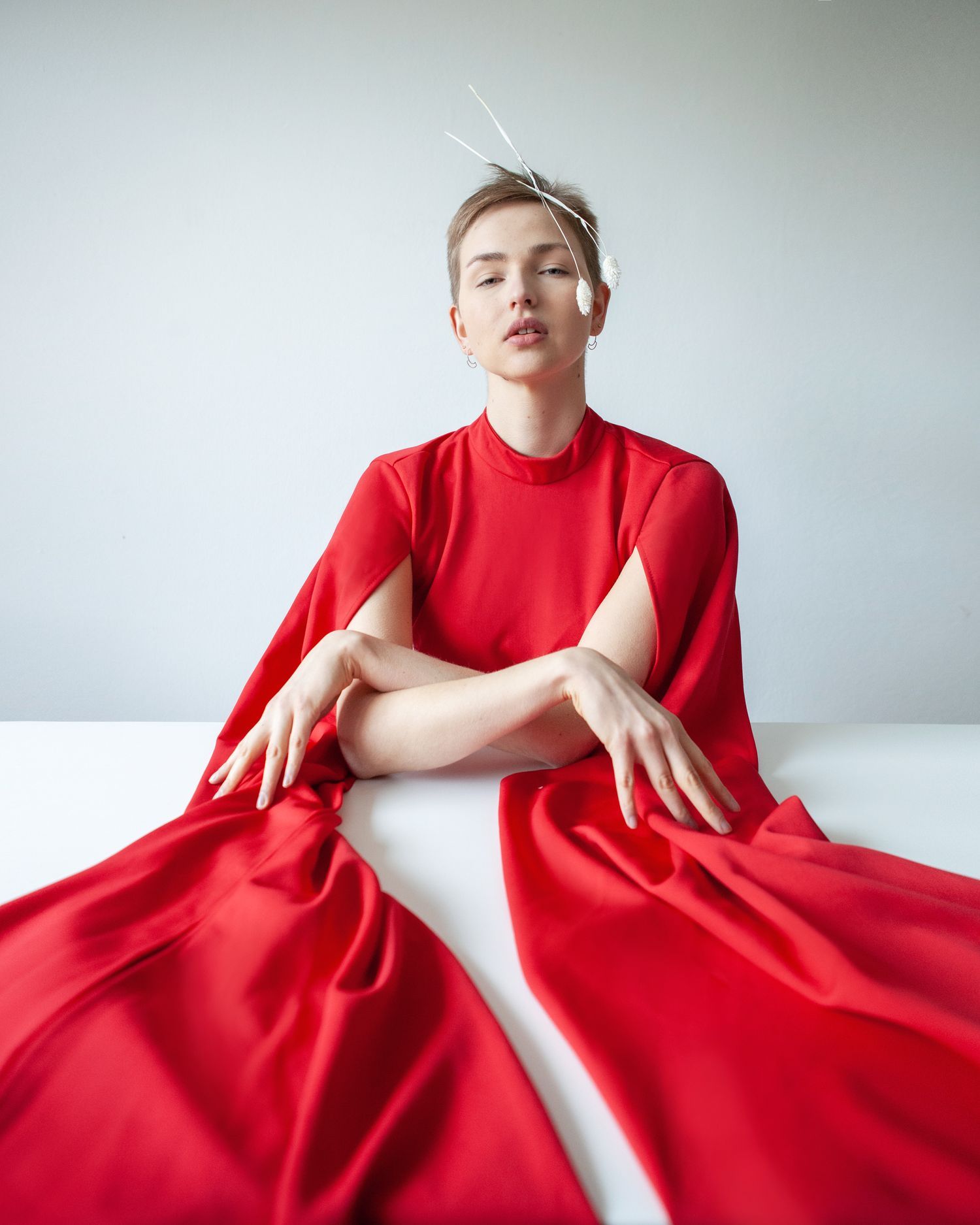 Fashion photo of model in dramatic red dress seated at white table.