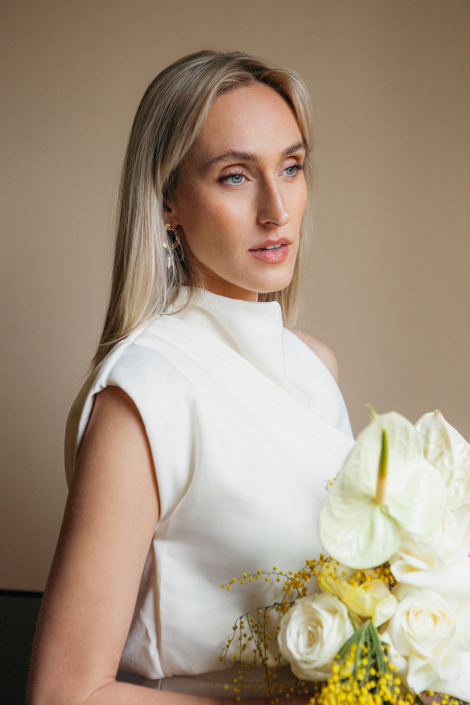 Portrait of bride in sleek white turtleneck dress holding cream and yellow bouquet.
