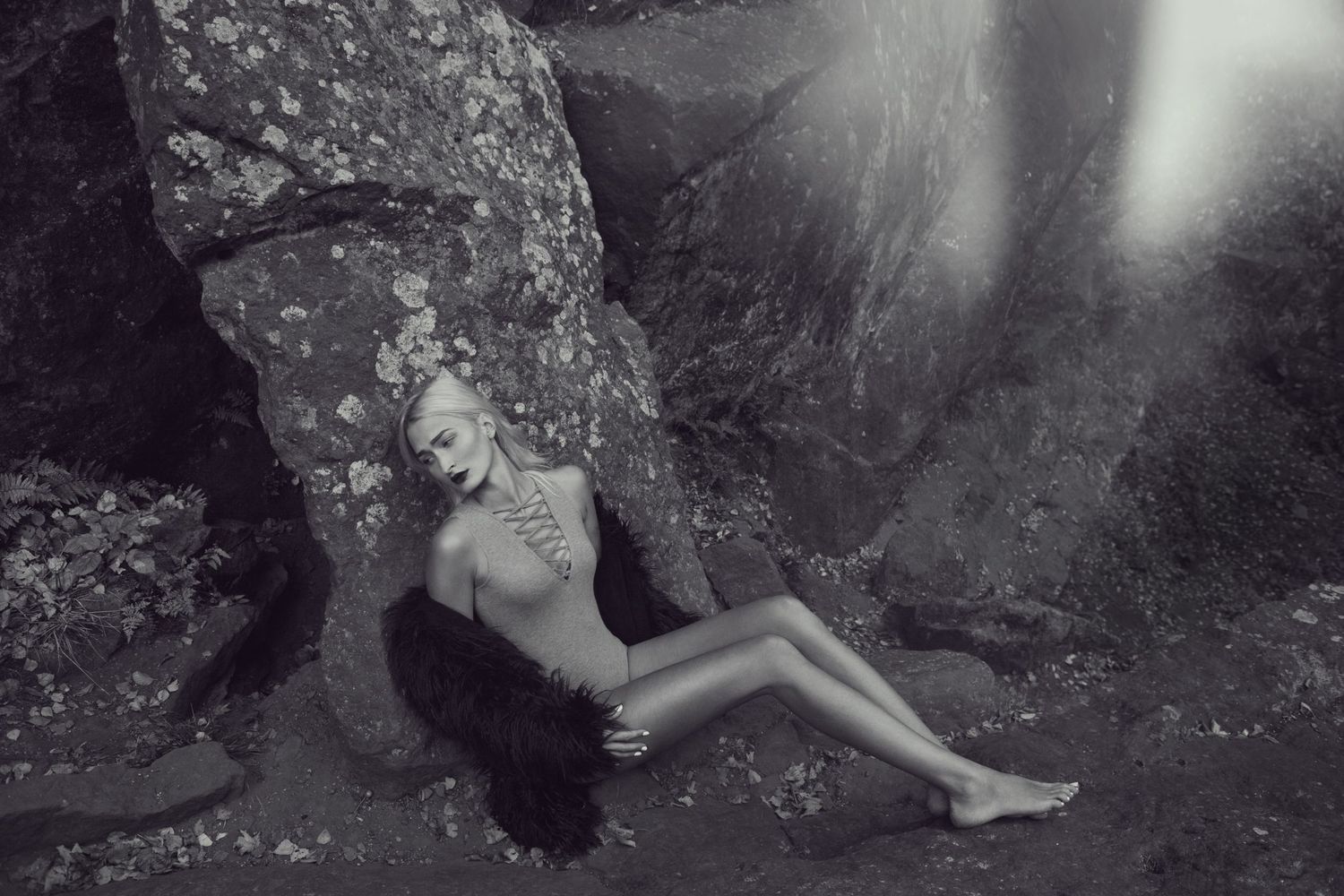 Monochrome fashion photo of a person reclining on rocky terrain near a waterfall.
