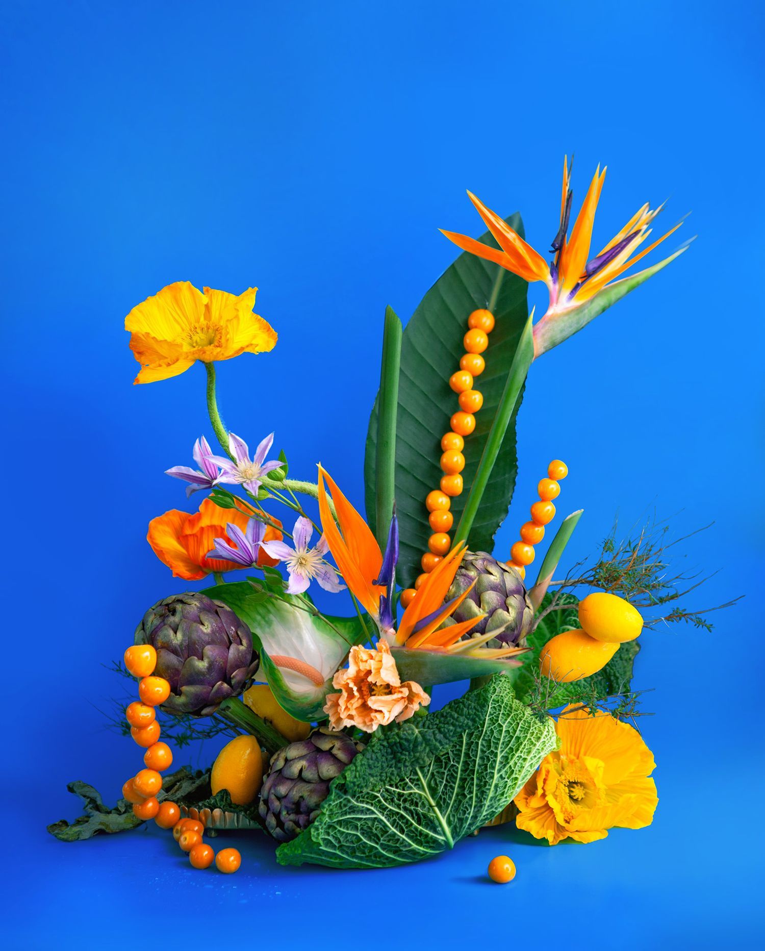 Tropical floral arrangement with bird of paradise flowers and orange berries against bright blue background.