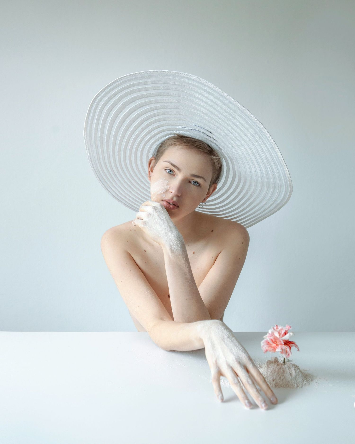 Elegant portrait wearing wide-brimmed white hat with pink flower accent.