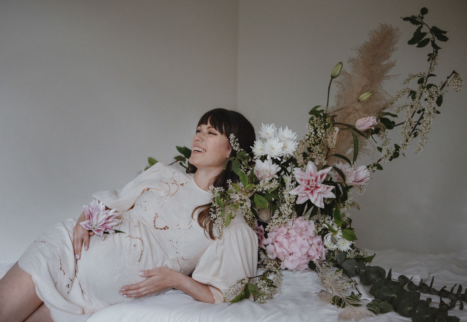 A dreamy portrait with soft pink floral arrangements and ethereal white fabric creating a romantic mood.