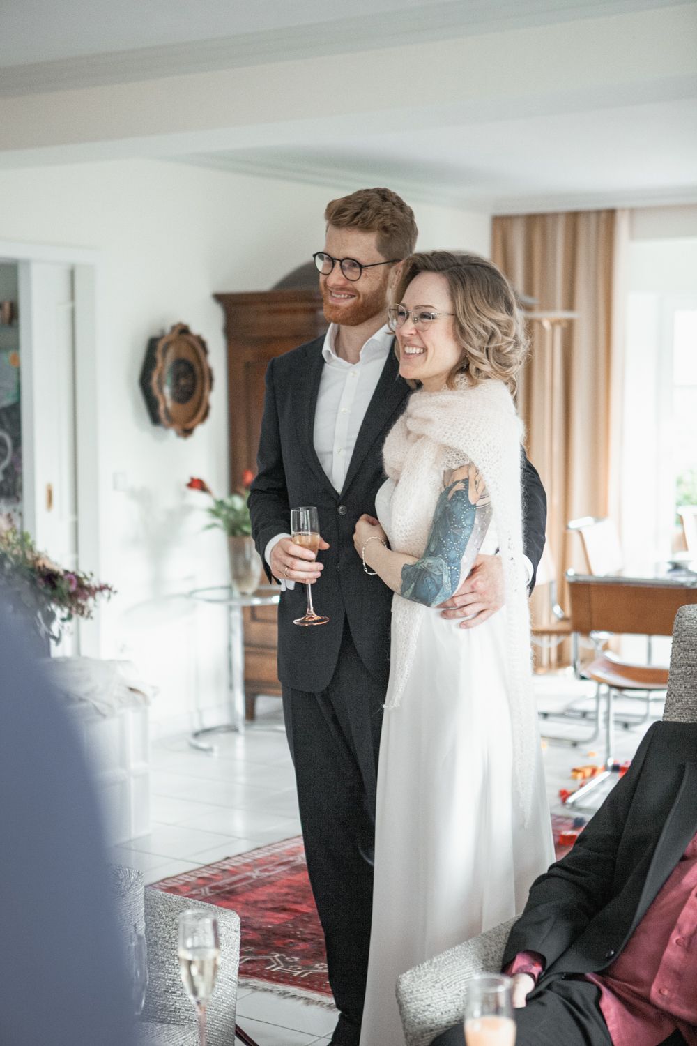 A couple in wedding attire share a tender moment while holding champagne glasses in an elegant indoor setting.