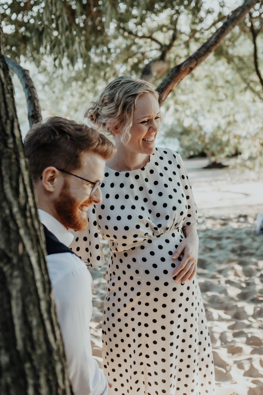 Couple shares intimate moment among trees on sandy beach path.