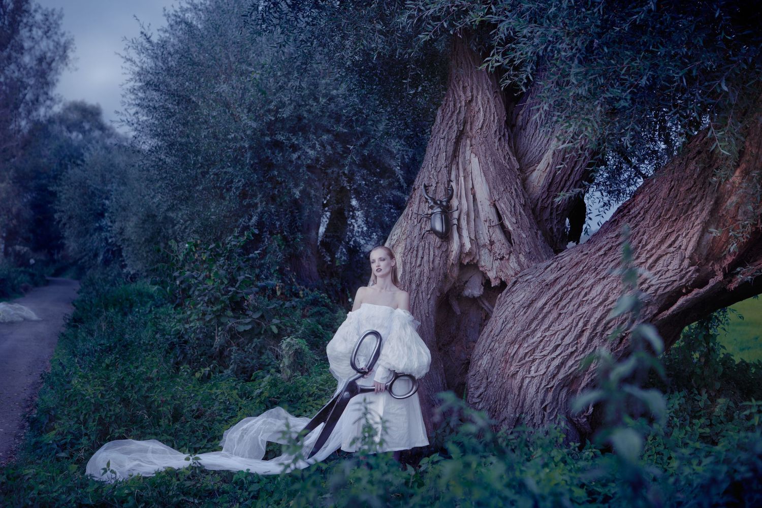 Dreamy scene of figure in white dress resting against large tree trunk at twilight.