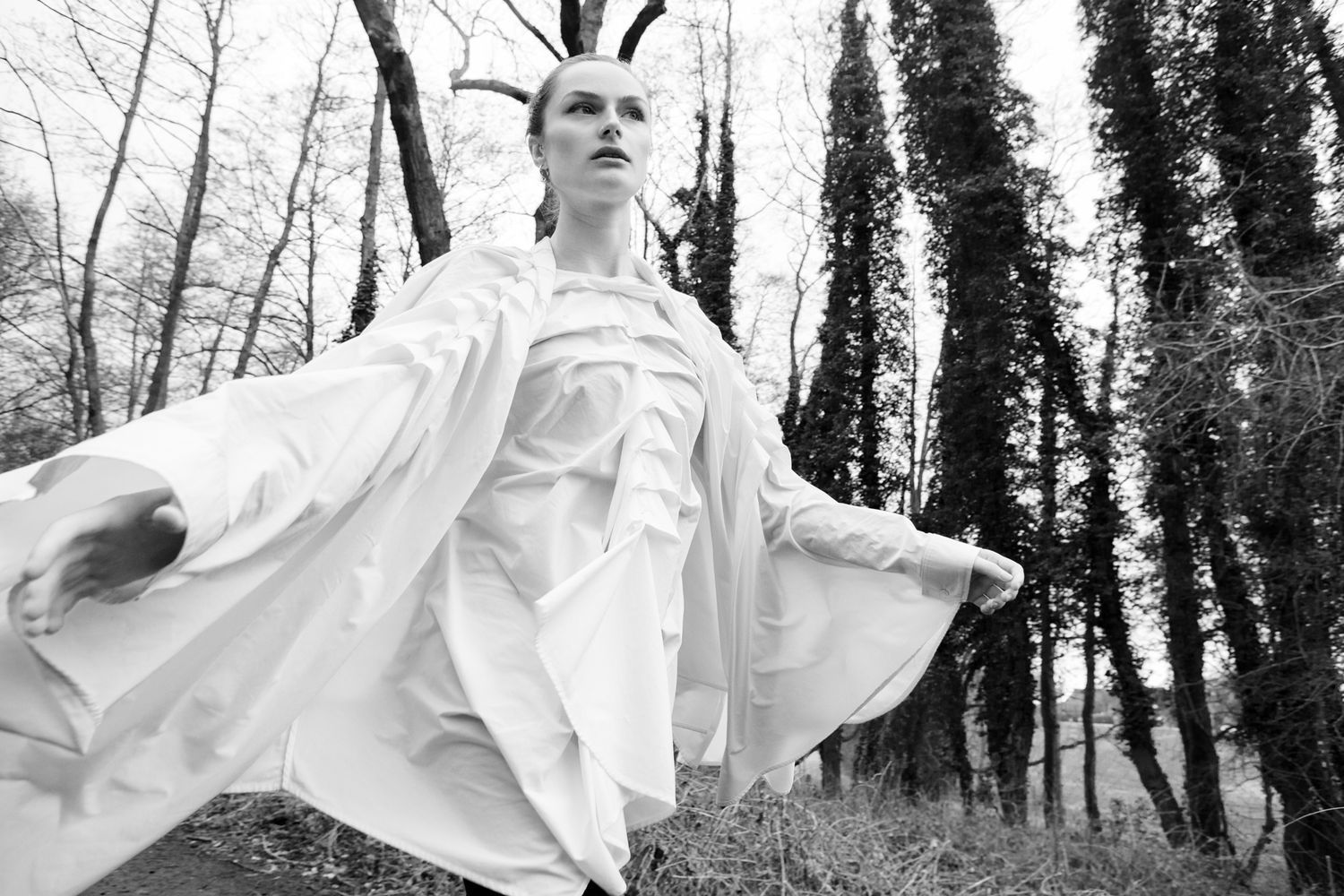 Fashion shot of flowing white garments against dark forest backdrop.