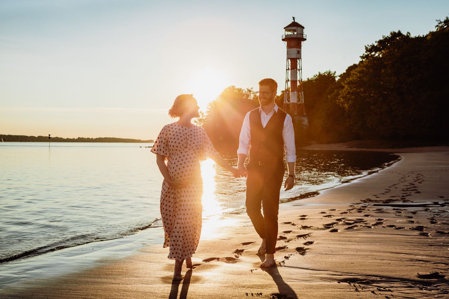 Romantic sunset beach walk with a lighthouse in the background creating a golden silhouette.