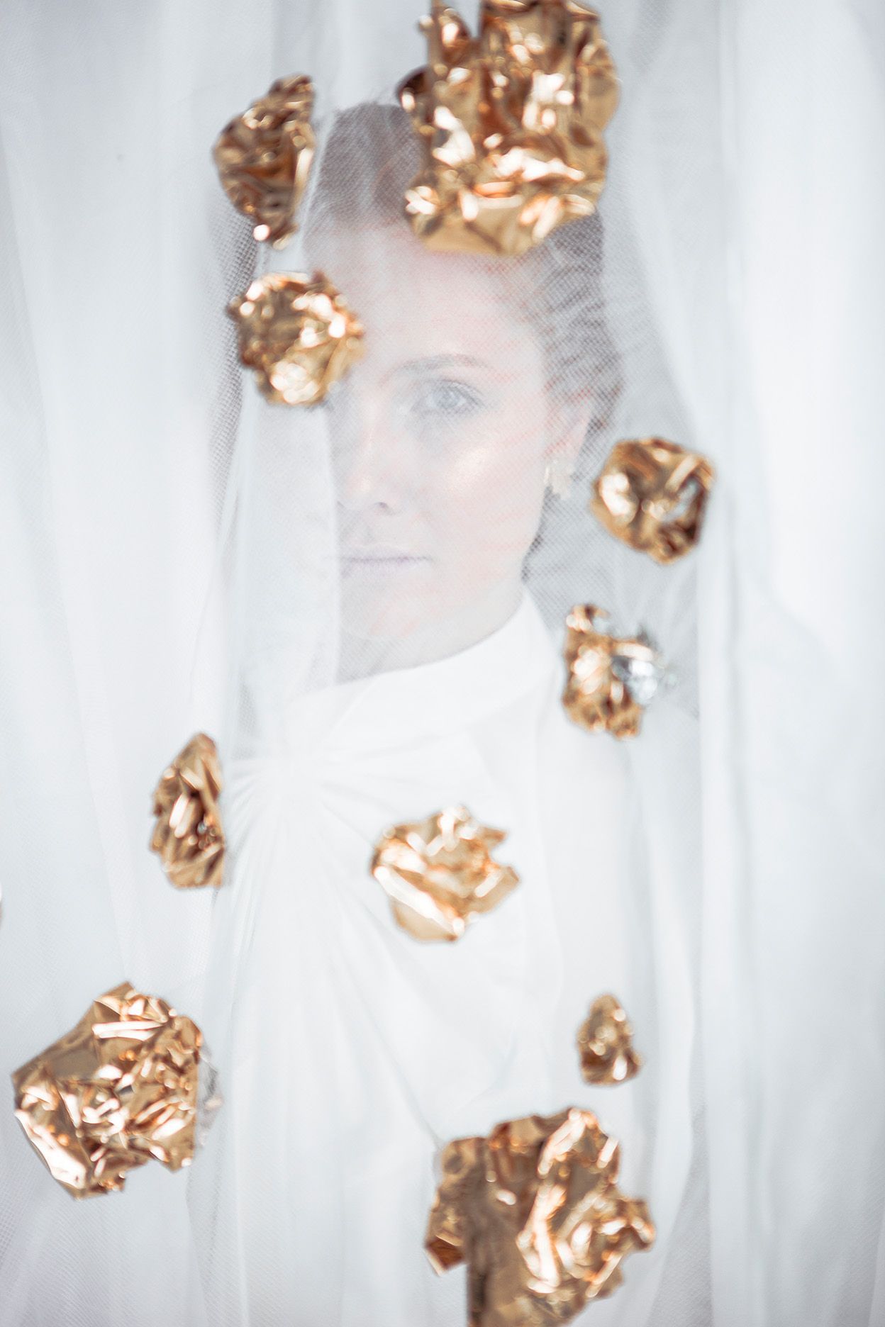 Portrait through sheer fabric with decorative gold elements creating ethereal artistic effect.