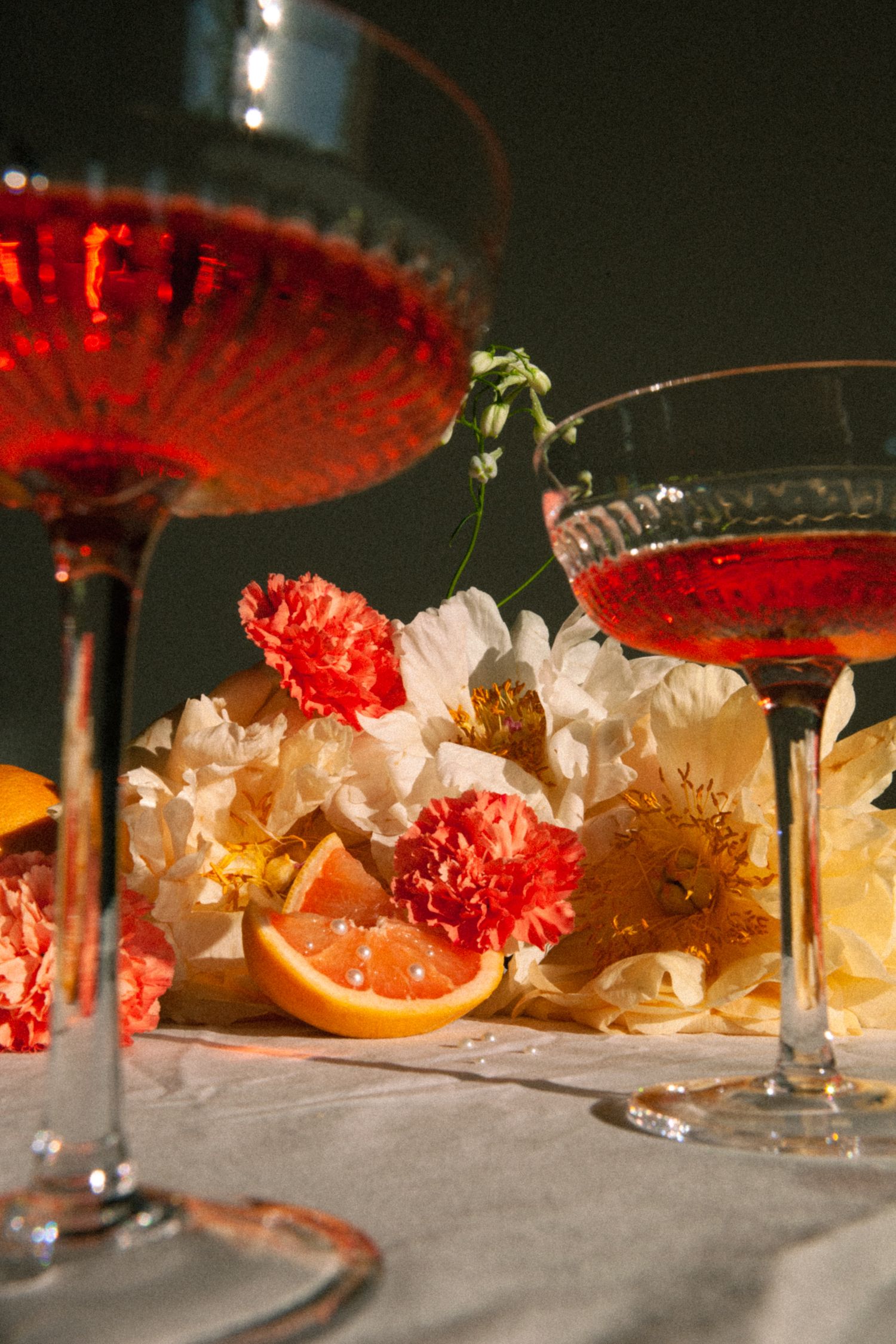 Close-up of red cocktails in crystal glasses with citrus and floral decorations.