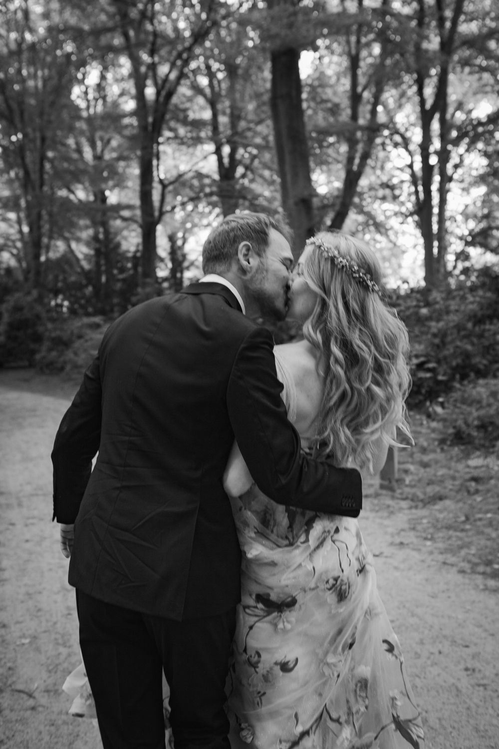 Black and white photo sequence of a romantic couple walking away on a wooded path in formal wedding attire.