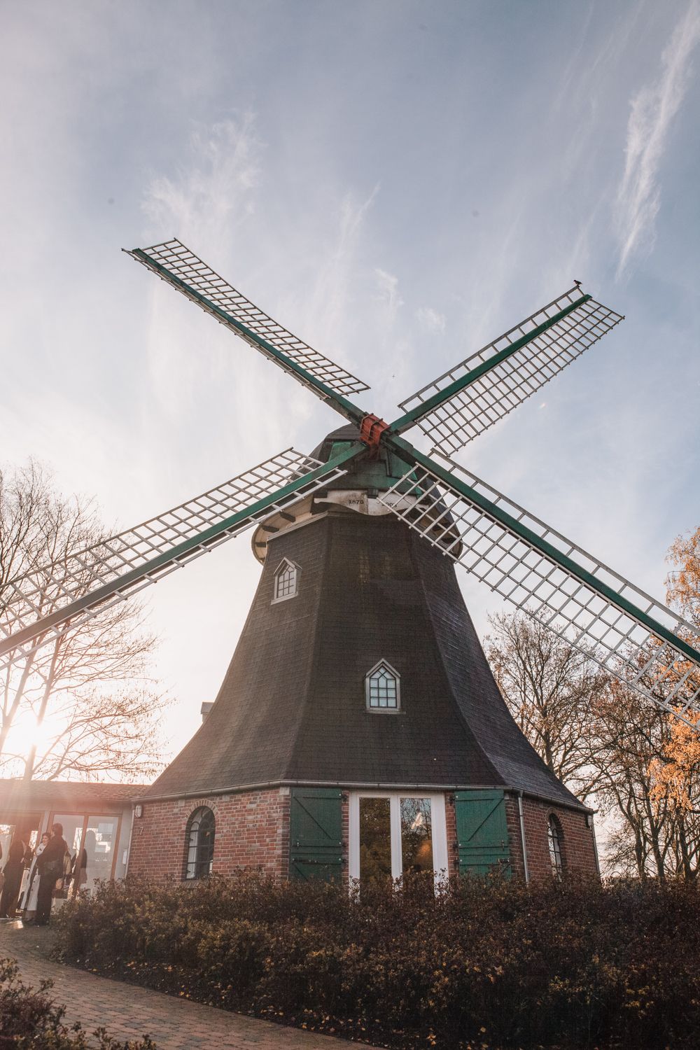 Traditional Dutch windmill with dark wooden structure and white sails against a misty autumn sky at sunset.