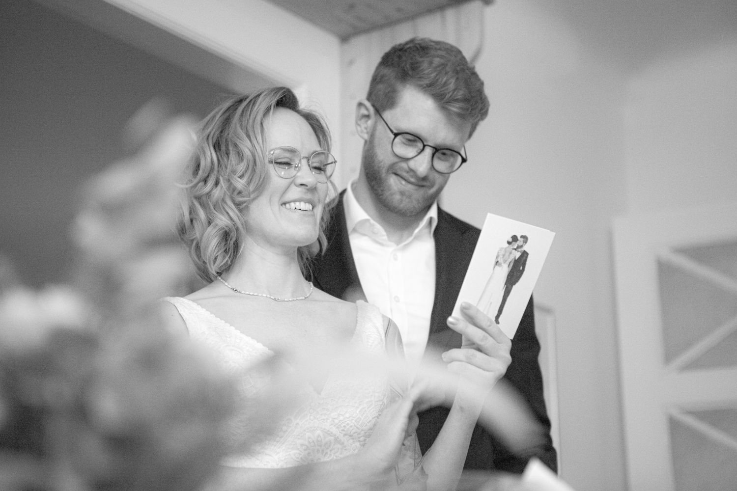Couple in black and white photo smiling together while looking at a small photo illustration or drawing.