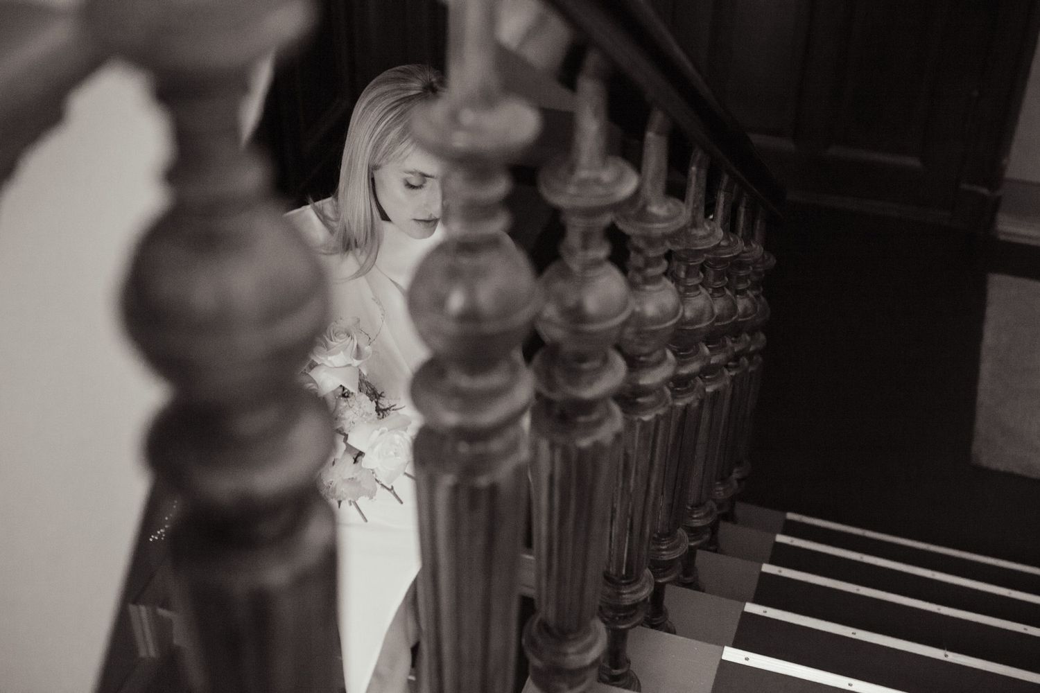 Artistic black and white photo of person with flowers between vintage stair railings.