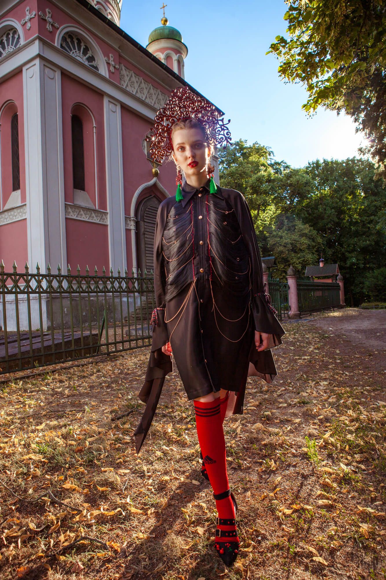 Gothic-inspired fashion look with red accents photographed in front of a pink Orthodox church.