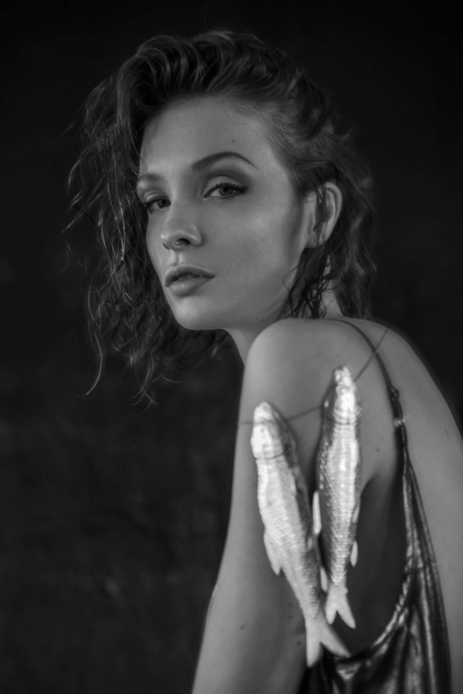 Dramatic black and white portrait with silver fish decorative elements against dark background.