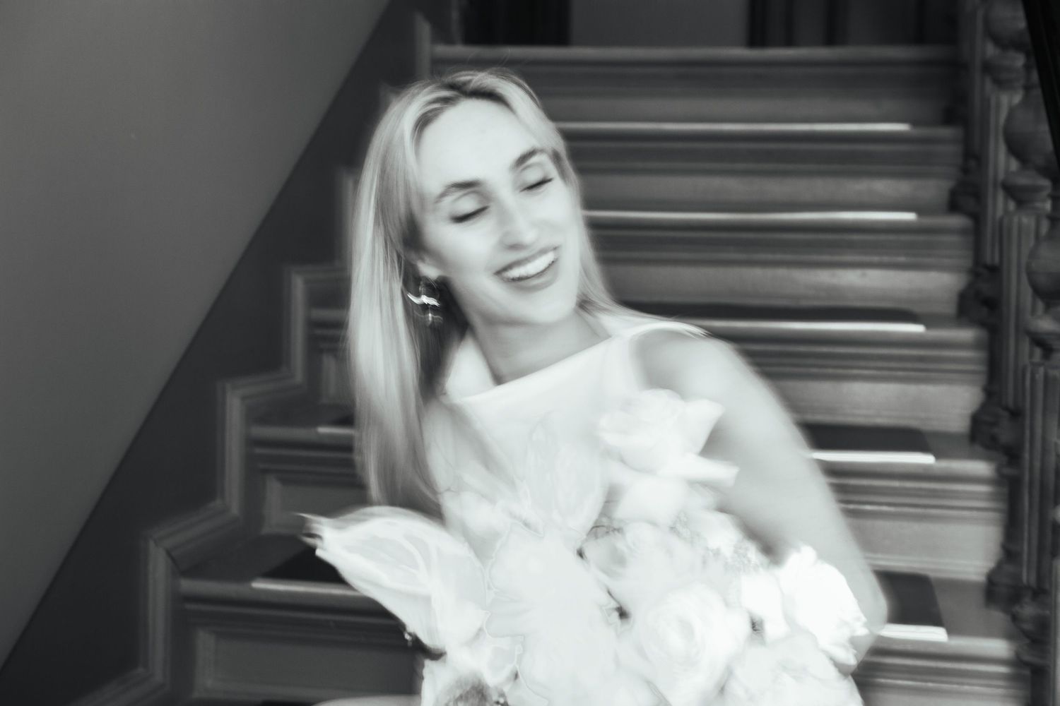 Joyful moment captured in black and white as woman laughs on staircase holding bouquet.