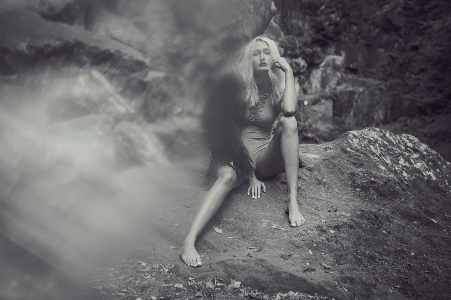 Dramatic black and white image of a figure in mist sitting on rocky terrain.