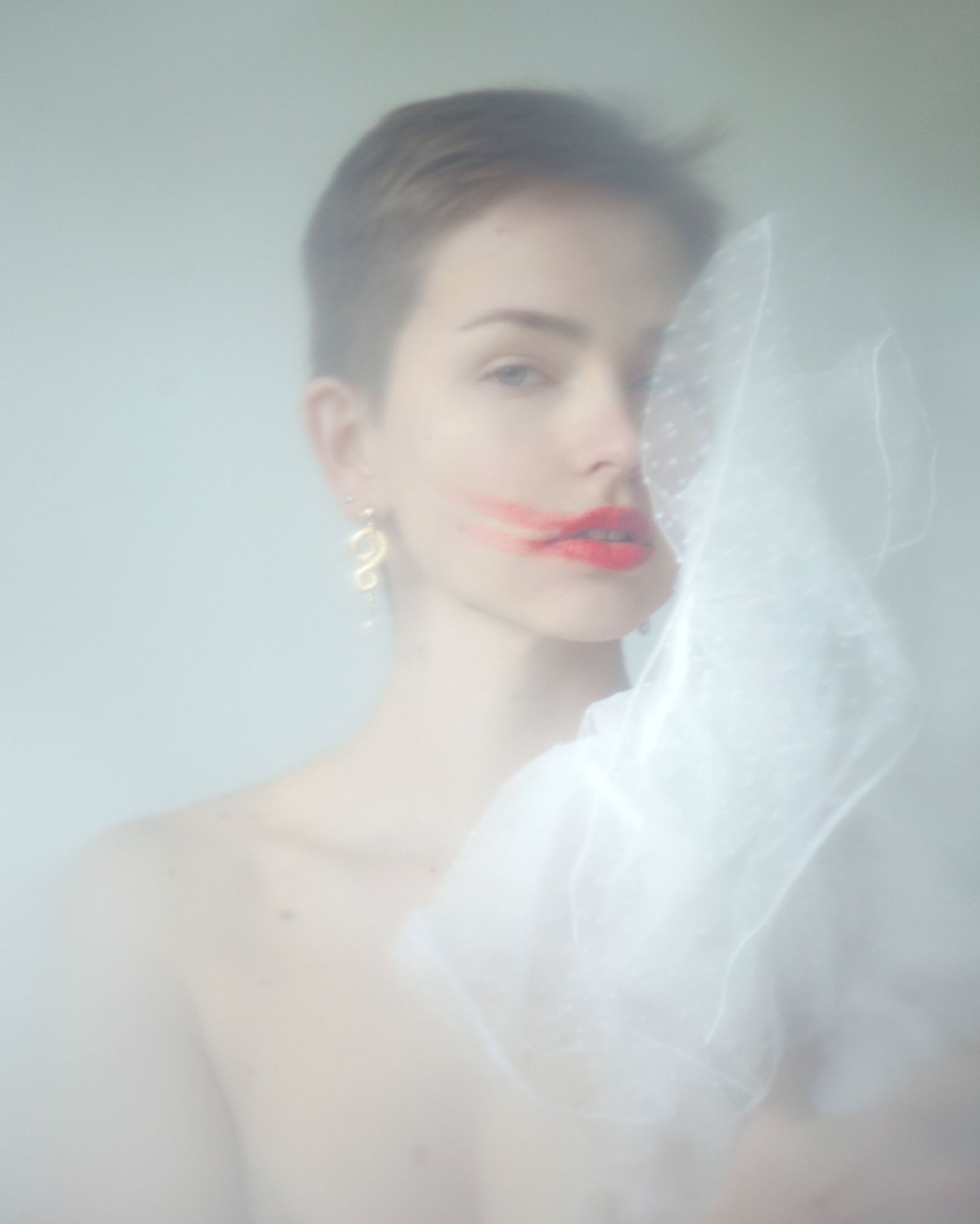 Dreamy portrait through sheer fabric with red lips and statement earring.